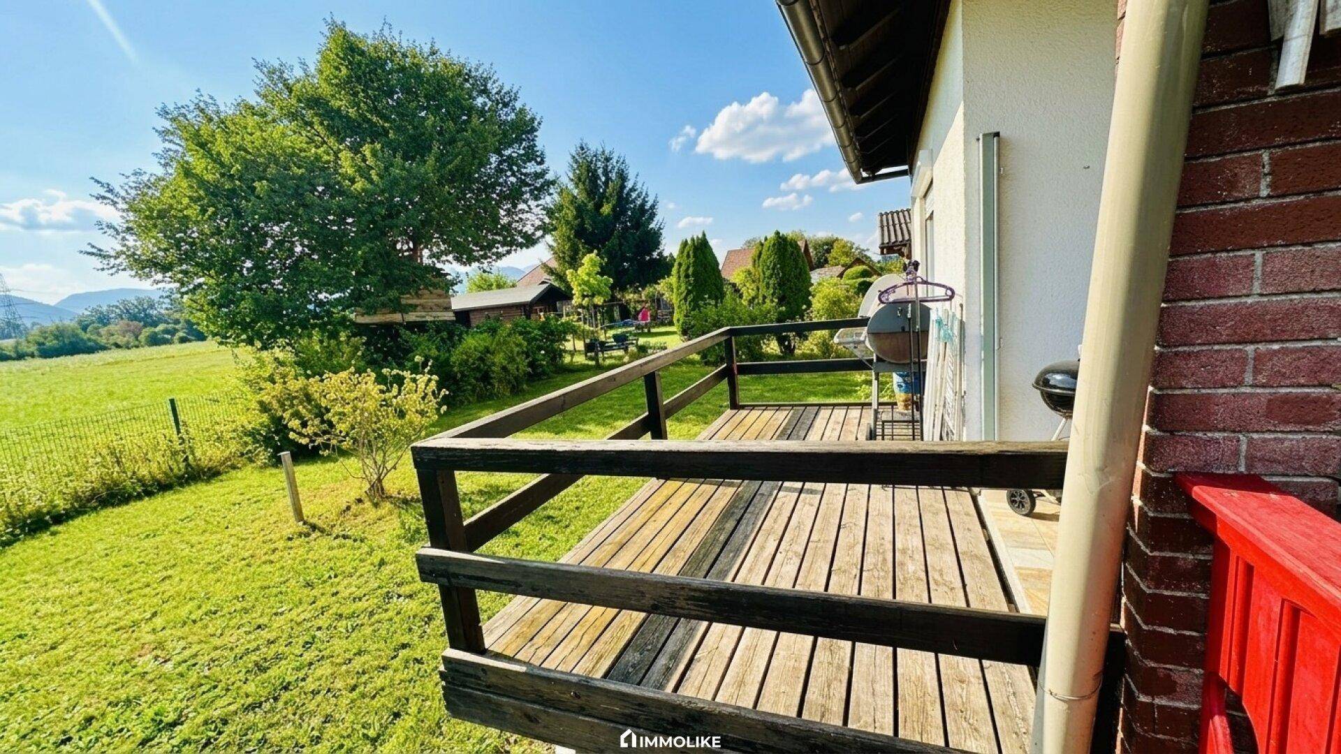Holzterrasse mit Grillbereich und Blick auf den grünen Garten und die umliegende Landschaft.