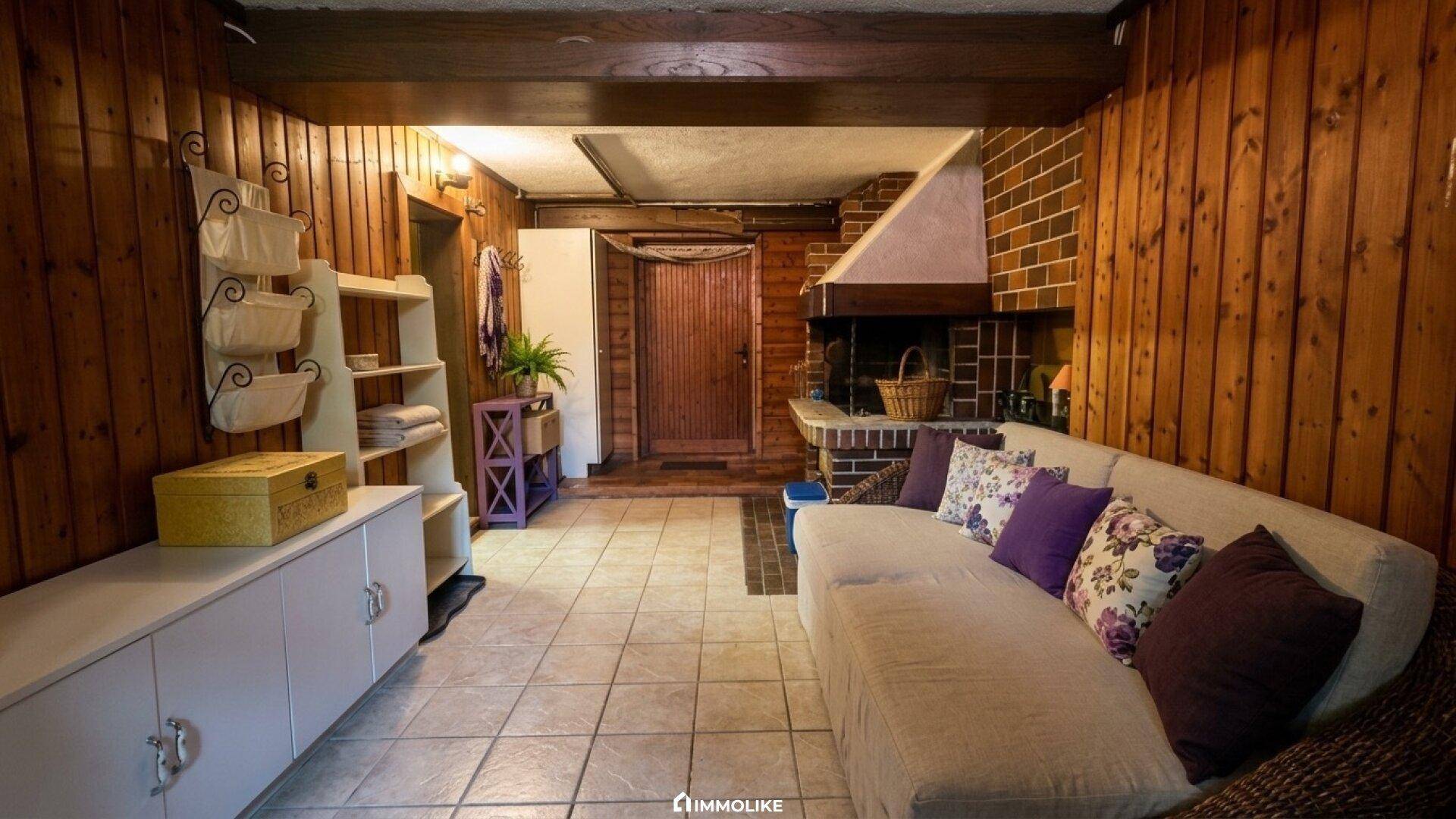 Gemütliches Wohnzimmer mit Holzvertäfelung, Fliesenboden und einem gemauerten Kamin.
