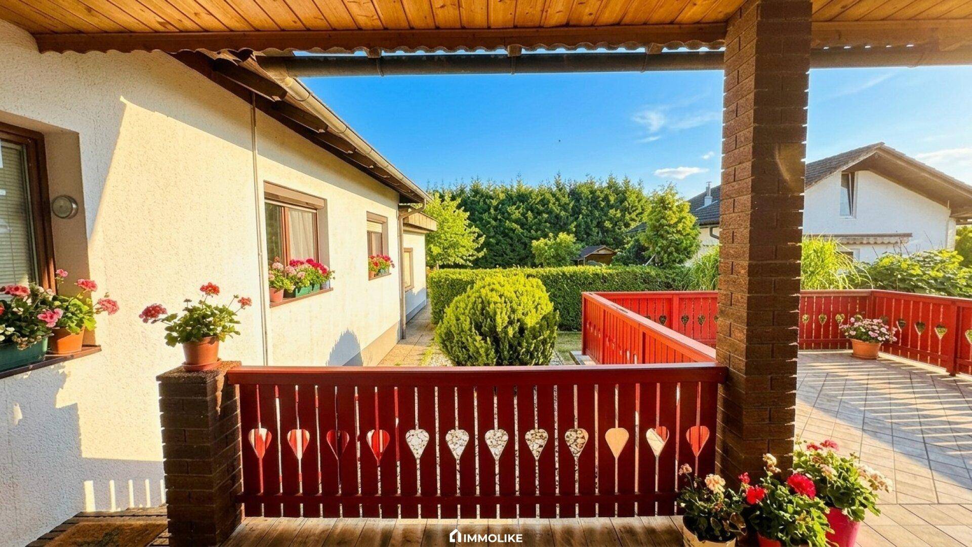Überdachter Balkon mit dekorativem roten Geländer und Blick in den Garten.