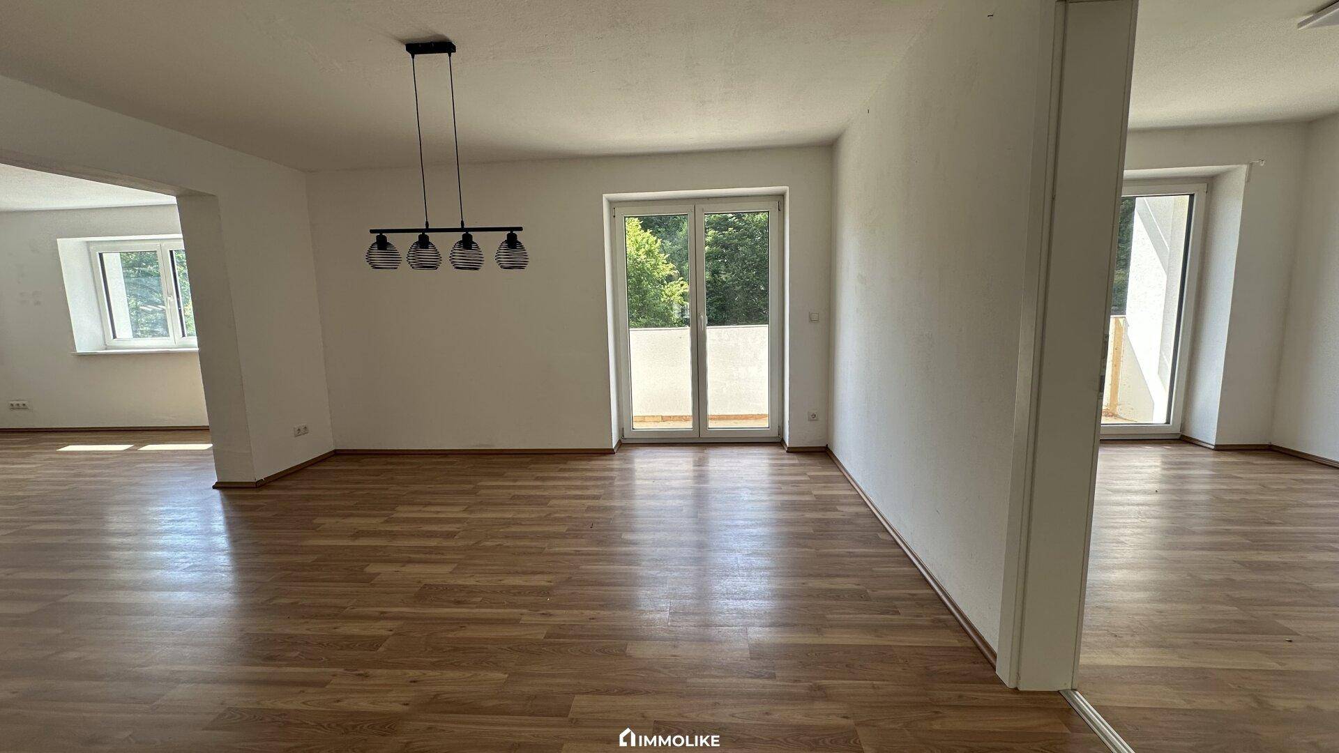 Geräumiger Wohnbereich mit Laminatboden, hellen Wänden und großen Fenstertüren zum Außenbereich.
