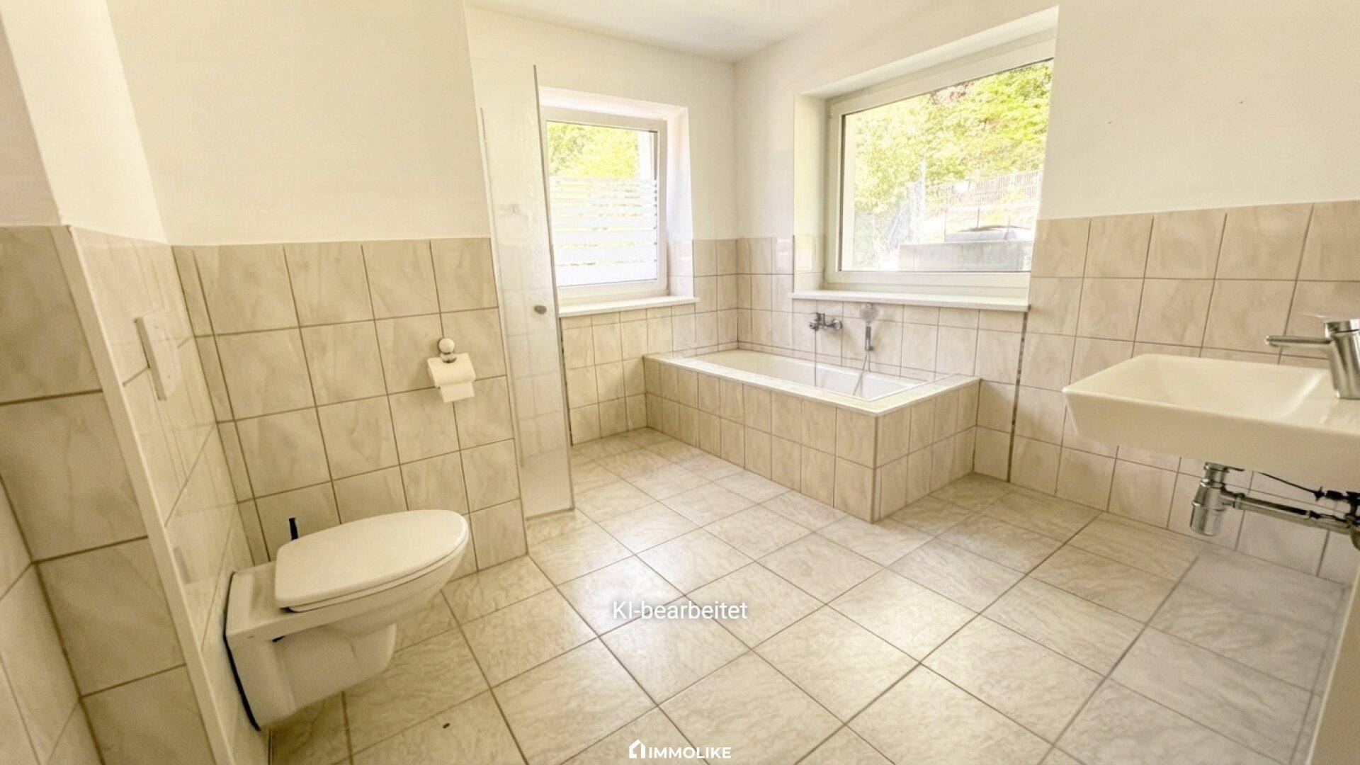 Helles Badezimmer mit Badewanne, WC, Waschbecken und zwei Fenstern für Tageslicht.
