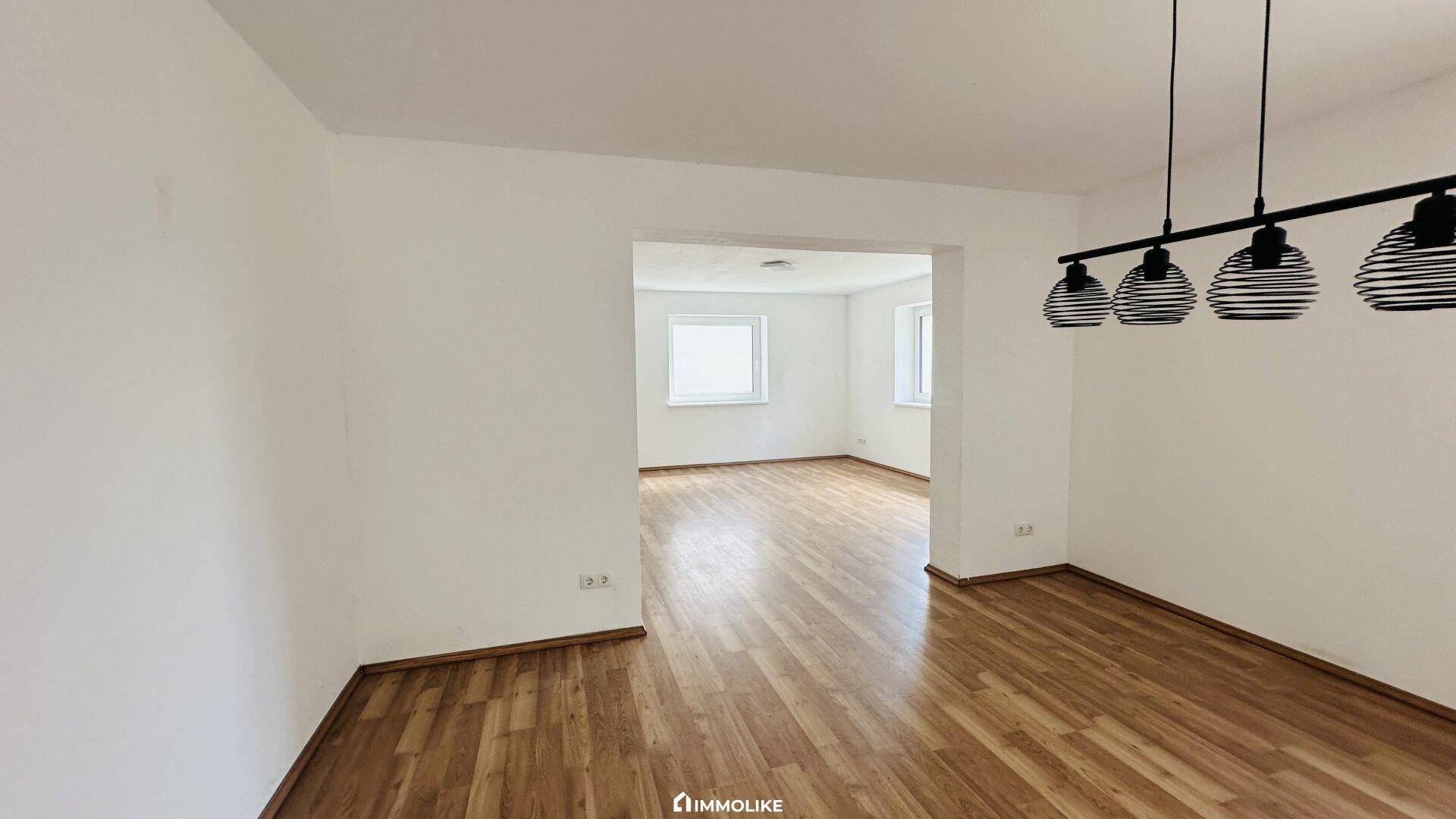 Offener Wohnbereich mit Laminatboden und hellen Wänden, bereit zur individuellen Gestaltung.