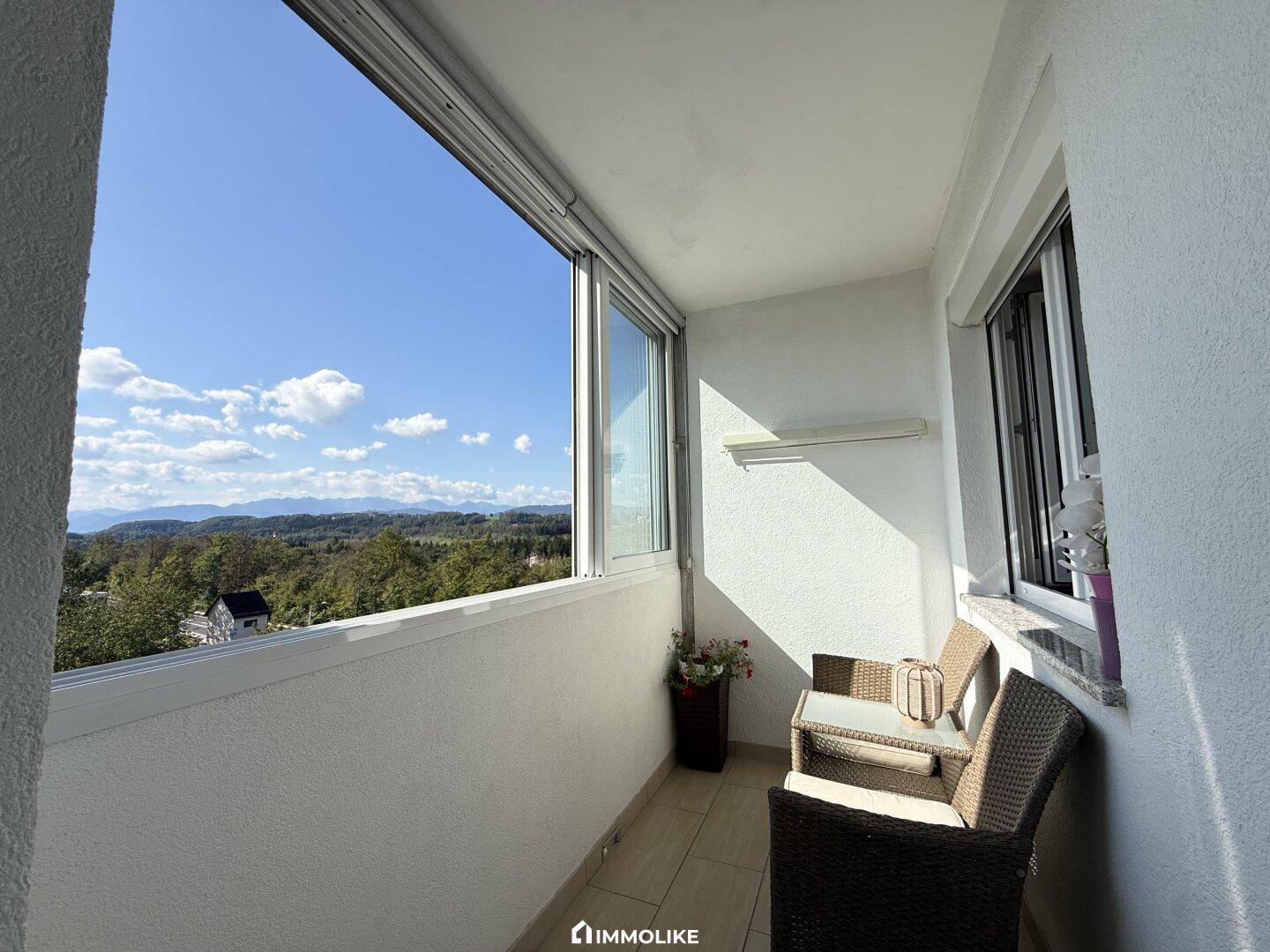 Verglaster Balkon mit Sitzgelegenheiten und weitem Blick auf die Berge und Landschaft.