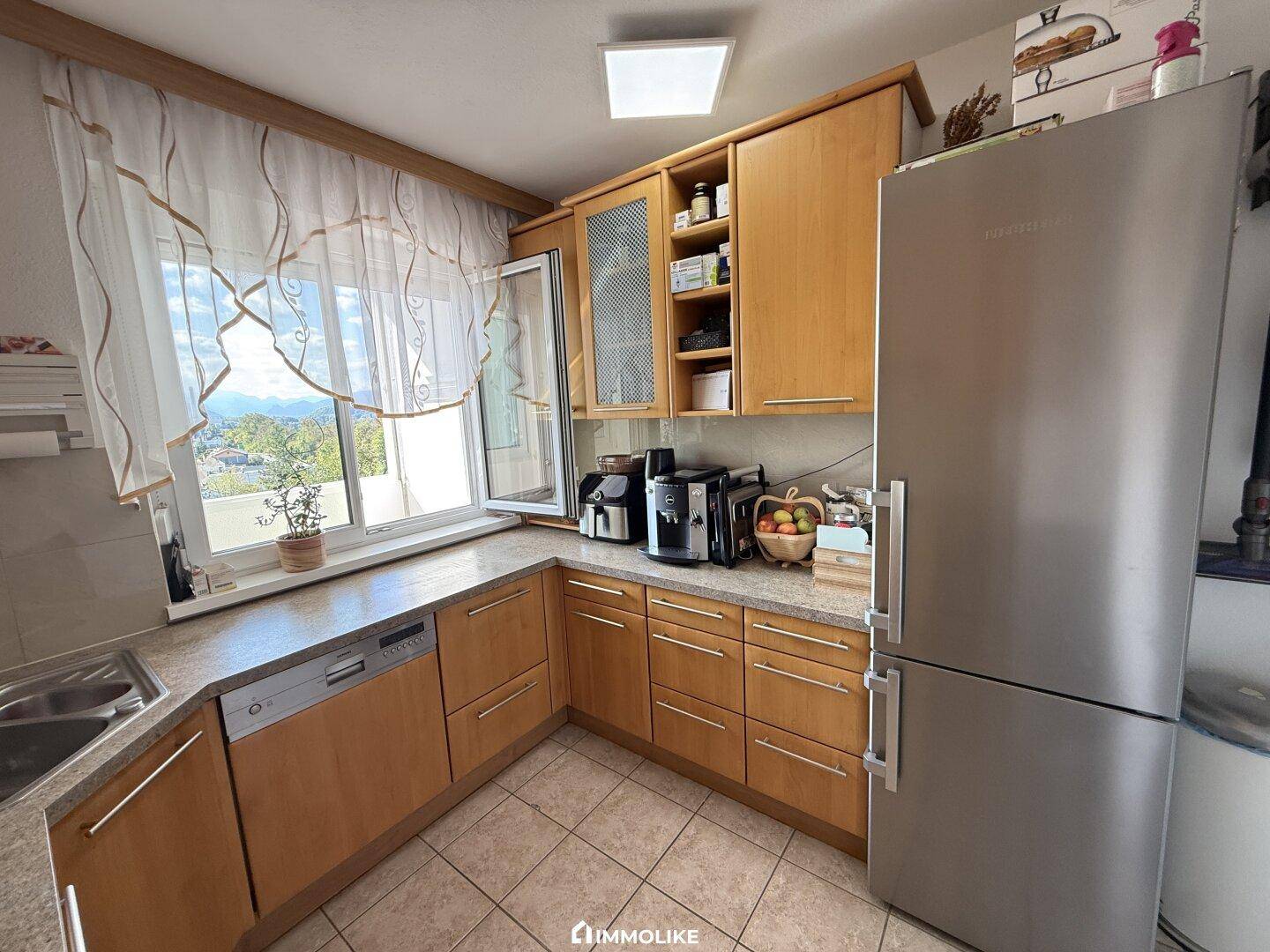 Gut ausgestattete Küche mit Holzfronten, Kühlschrank und Fenster mit schöner Aussicht.