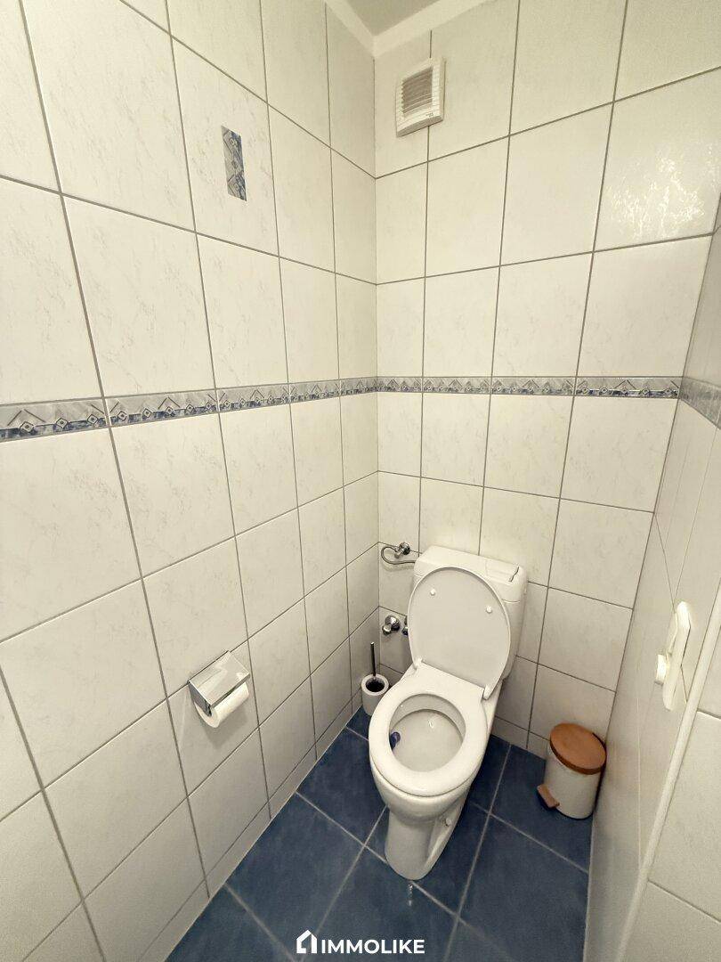 Separates WC mit weißen Fliesen und blauen Akzenten, ausgestattet mit Toilette.
