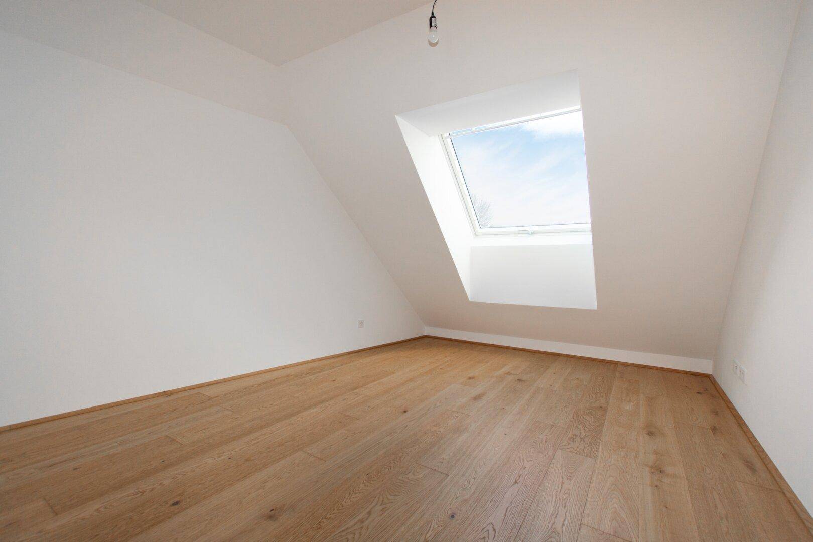 Gemütliches Dachzimmer mit einem großen Dachfenster und schrägen Wänden, perfekt für ein Kinderzimmer.