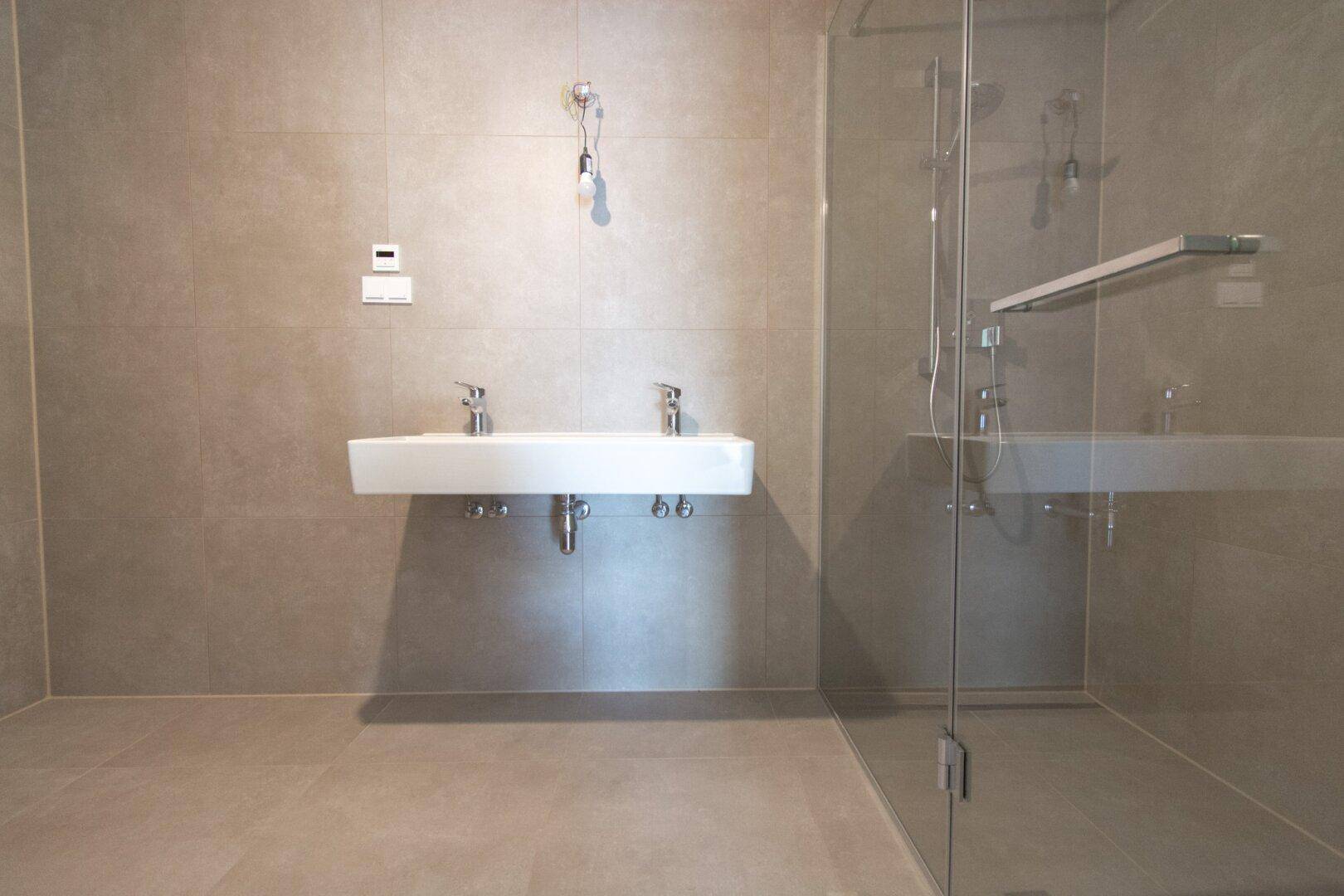 Modernes Badezimmer mit grauen Fliesen, Doppelwaschbecken und einer begehbaren Dusche.