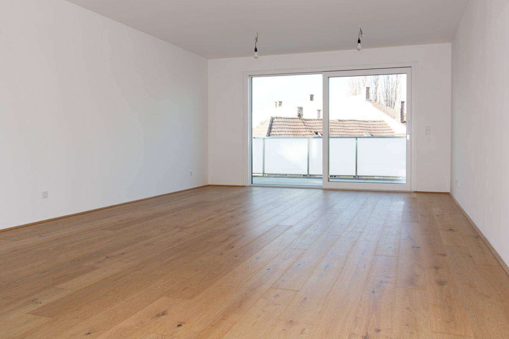 Heller Wohnraum mit Parkettboden und Zugang zu einem Balkon mit Blick auf die Dächer.