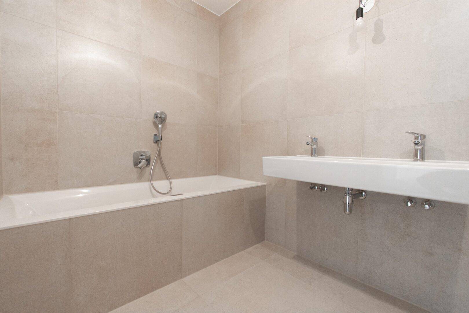 Modernes Badezimmer mit hellen Fliesen, einer Badewanne und einem Doppelwaschbecken.