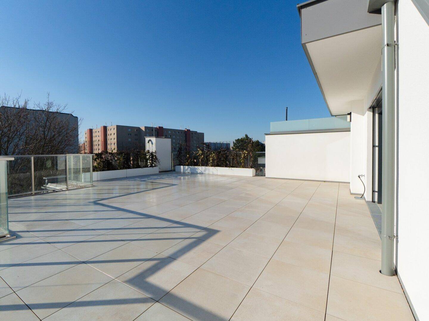 Große, sonnige Dachterrasse mit Fliesenboden und Blick auf die städtische Umgebung.