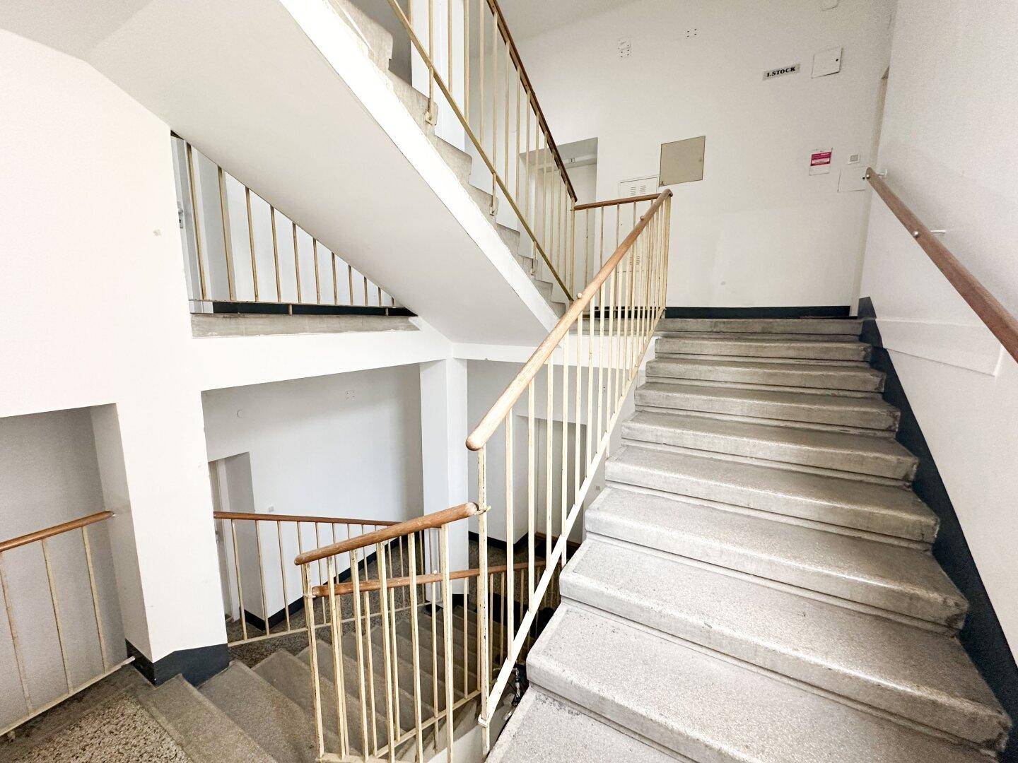 Helles Treppenhaus mit mehreren Etagen, Steinstufen und Metallgeländer in einem Mehrfamilienhaus.