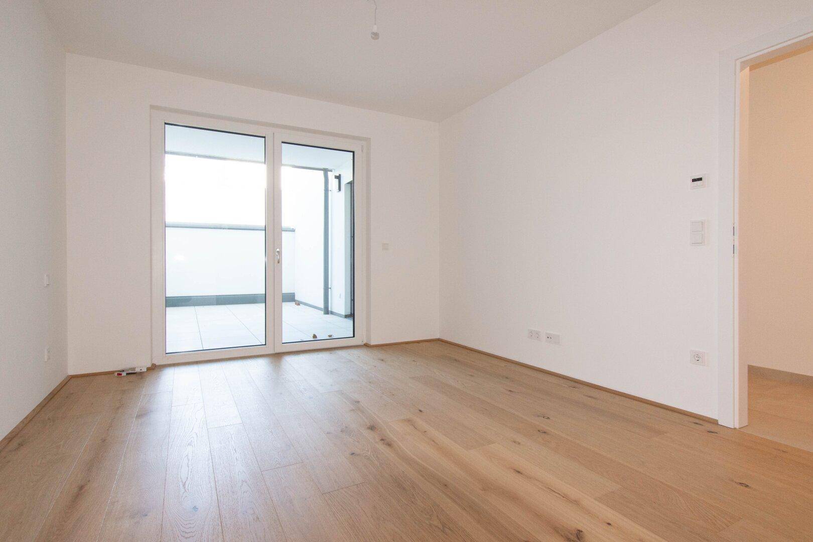 Helles Zimmer mit neuem Parkettboden und direktem Zugang zu einem Balkon.