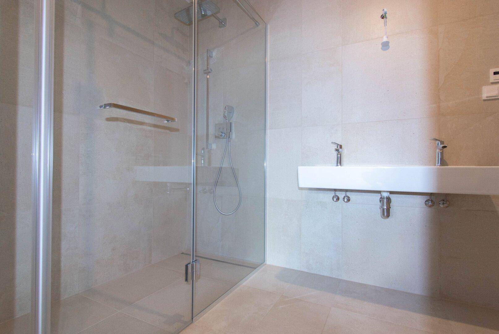 Modernes Badezimmer mit großer Glasdusche und Doppelwaschbecken, hell gefliest.