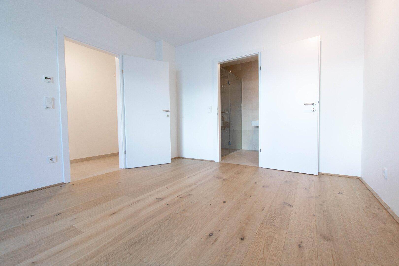 Geräumiges Zimmer mit hellem Parkettboden und Zugang zu einem weiteren Raum und Bad.