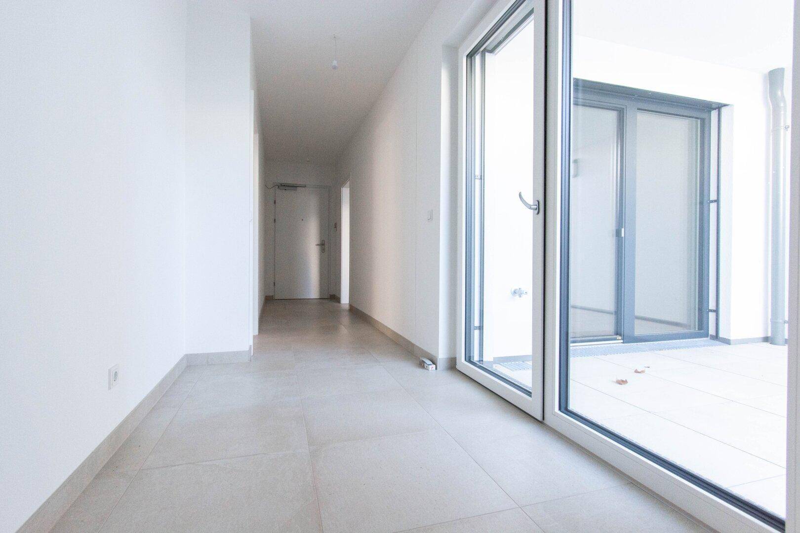 Heller Flur mit Fliesenboden und großem Fenster, das Zugang zu einem Außenbereich bietet.