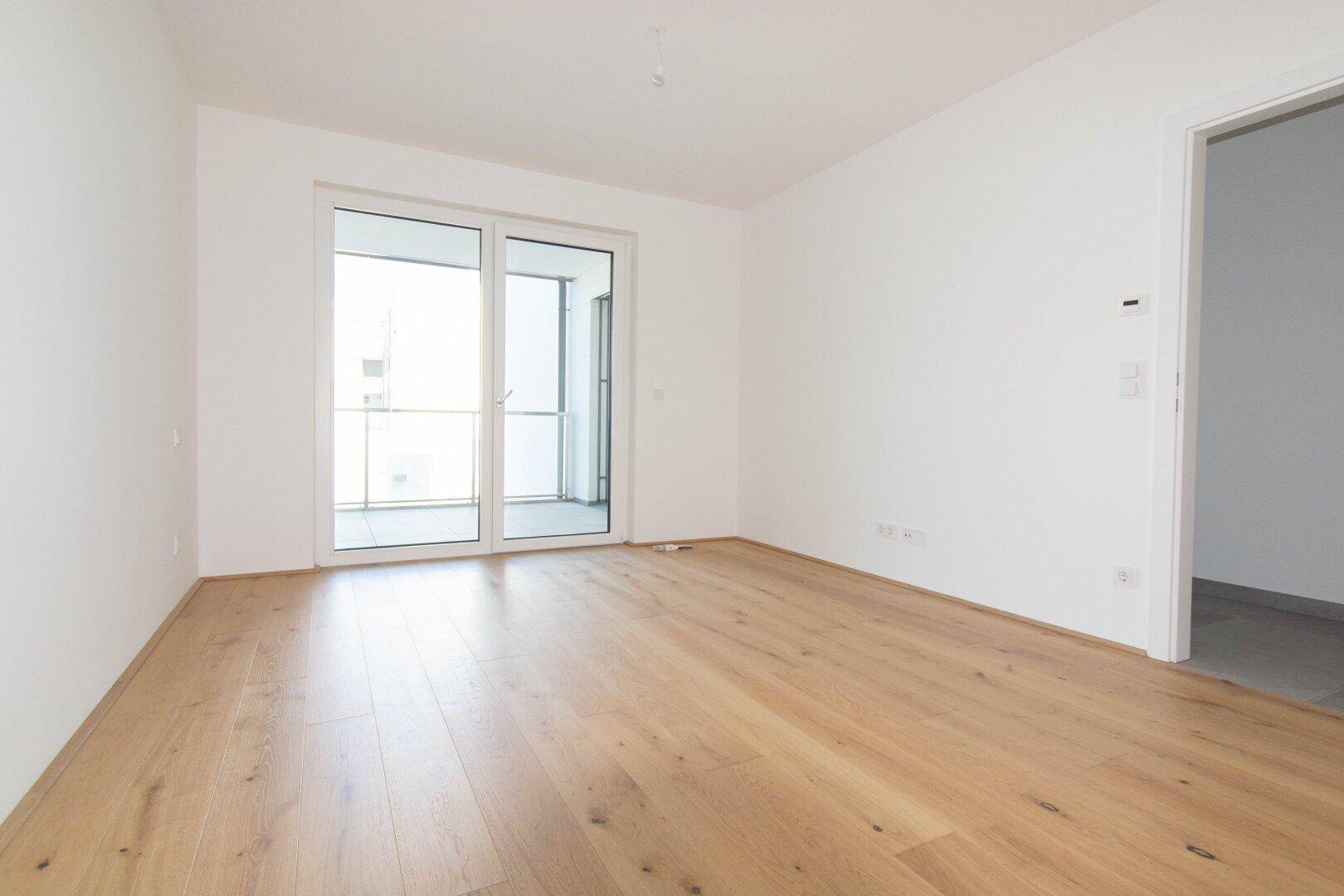 Geräumiges Zimmer mit Holzboden und Zugang zu einem Balkon, ideal als Wohnbereich.
