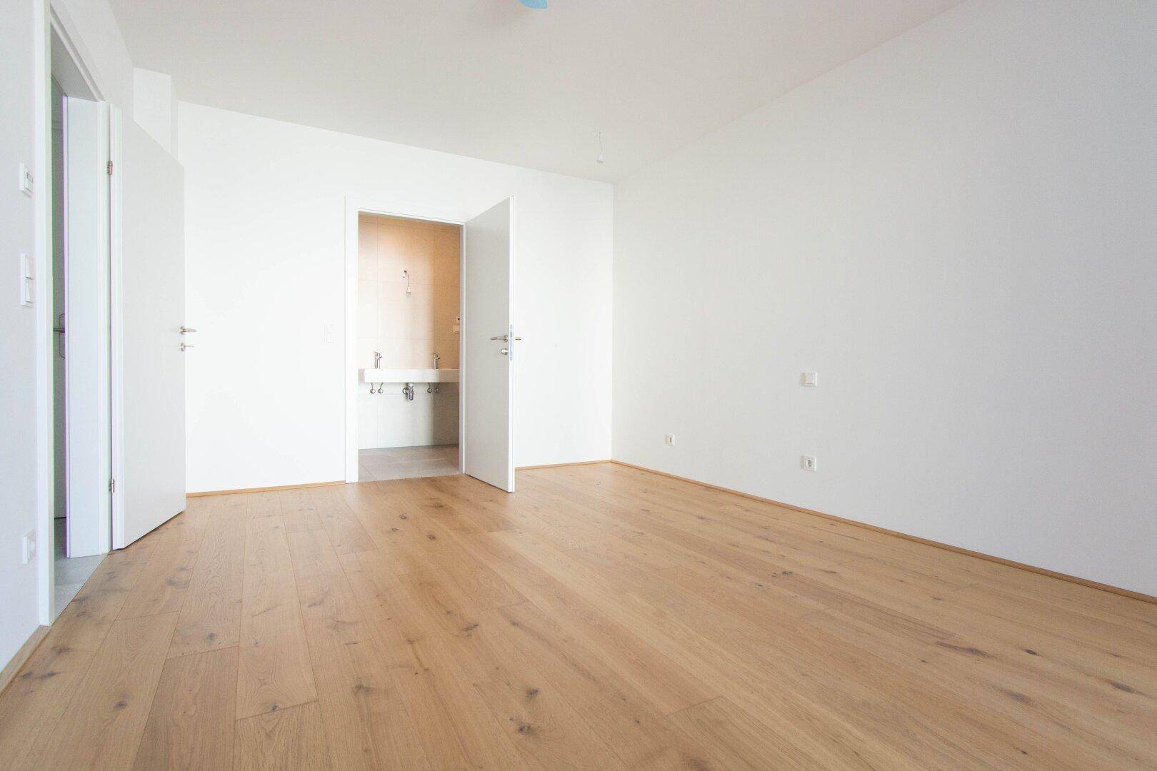 Helles Schlafzimmer mit Holzboden und integriertem Waschbereich, bereit zur individuellen Gestaltung.