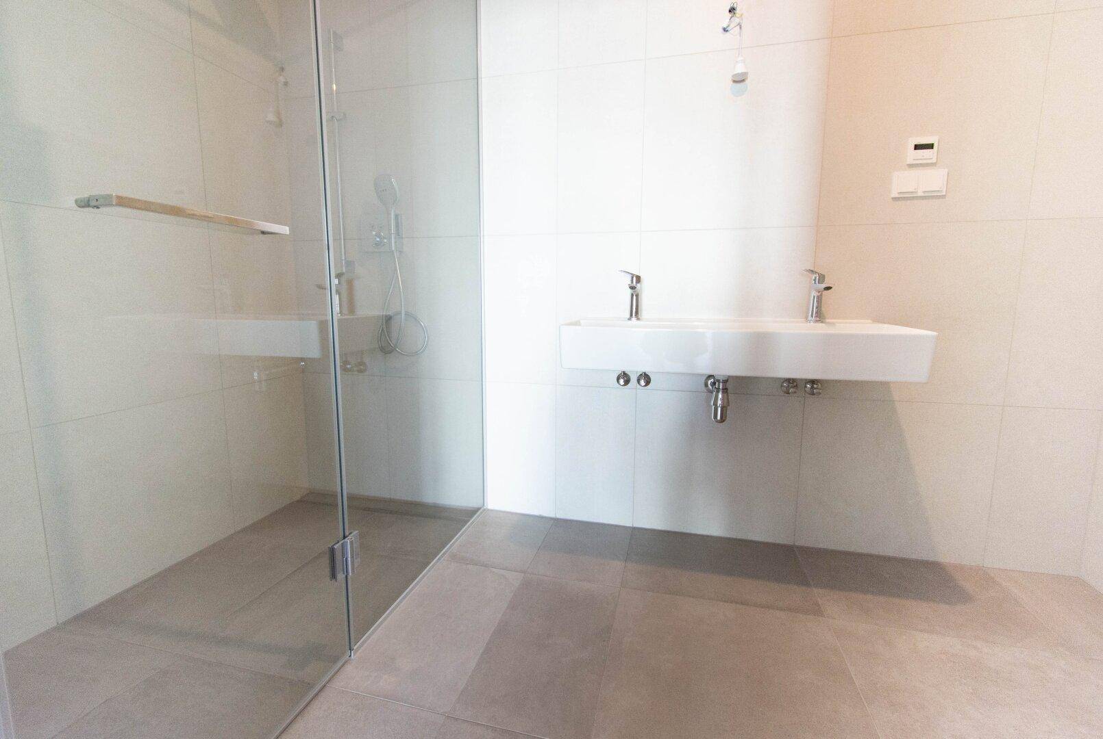 Modernes Badezimmer mit begehbarer Dusche, Doppelwaschbecken und hellen Fliesen.