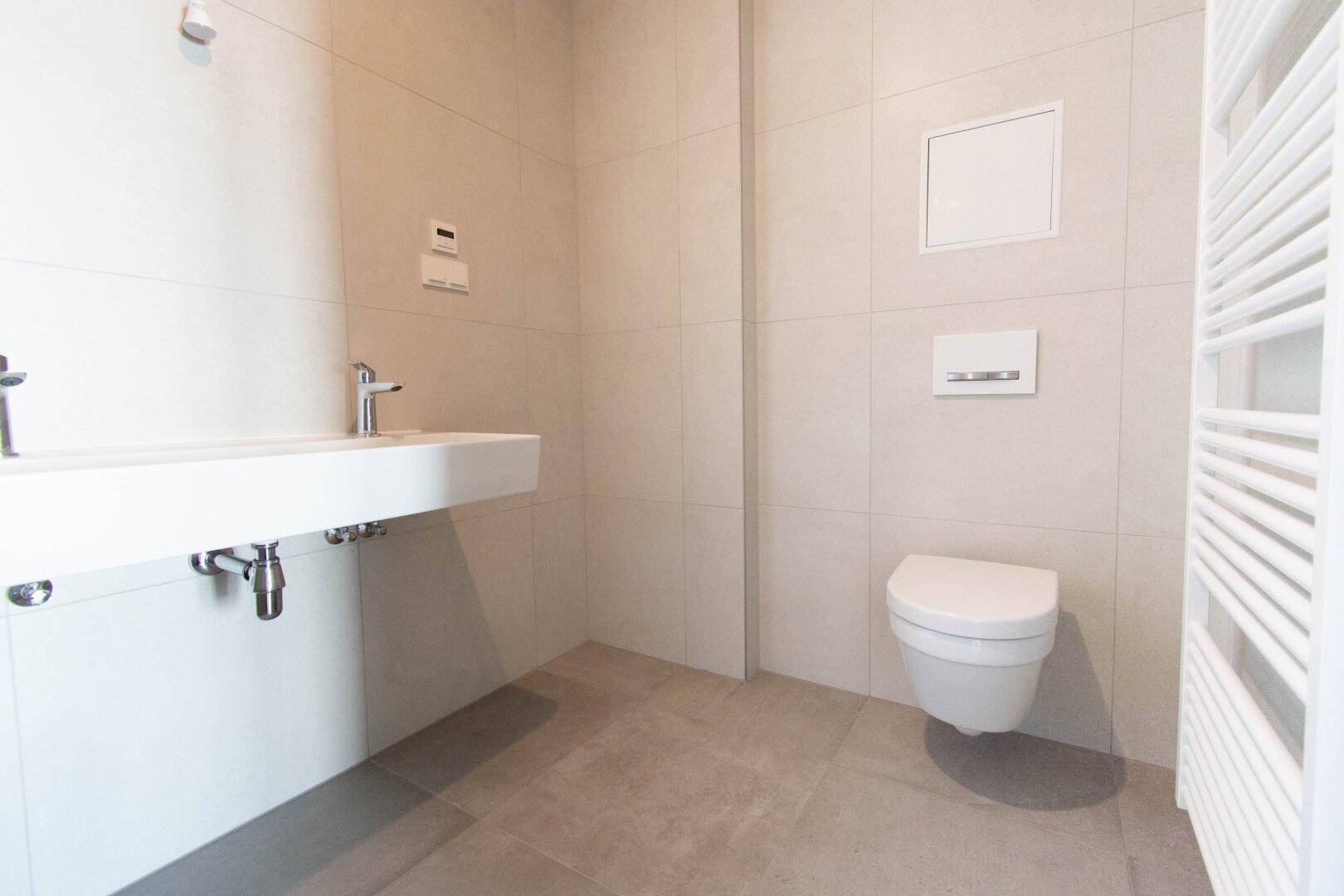 Modernes WC mit wandhängender Toilette, Waschbecken und beheiztem Handtuchhalter.