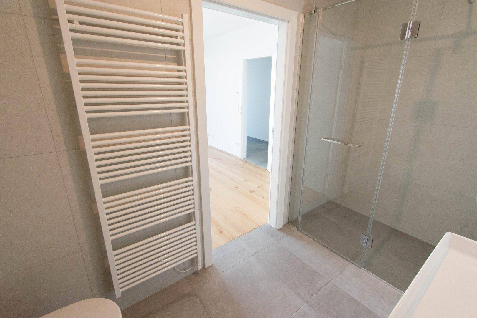 Badezimmer mit moderner Glasdusche und beheiztem Handtuchhalter, Blick in angrenzendes Zimmer.