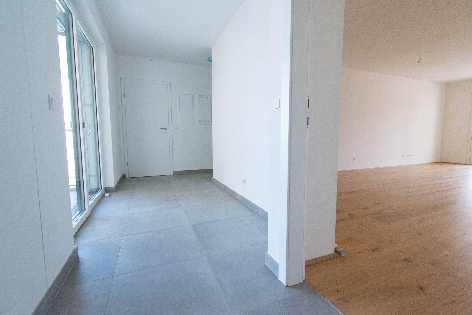 Heller Eingangsbereich mit Fliesenboden, der in einen offenen Wohnbereich übergeht.