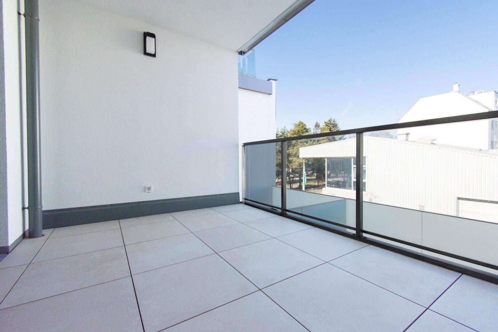Moderner Balkon mit Fliesenboden und Glasgeländer, bietet einen hellen Außenbereich.