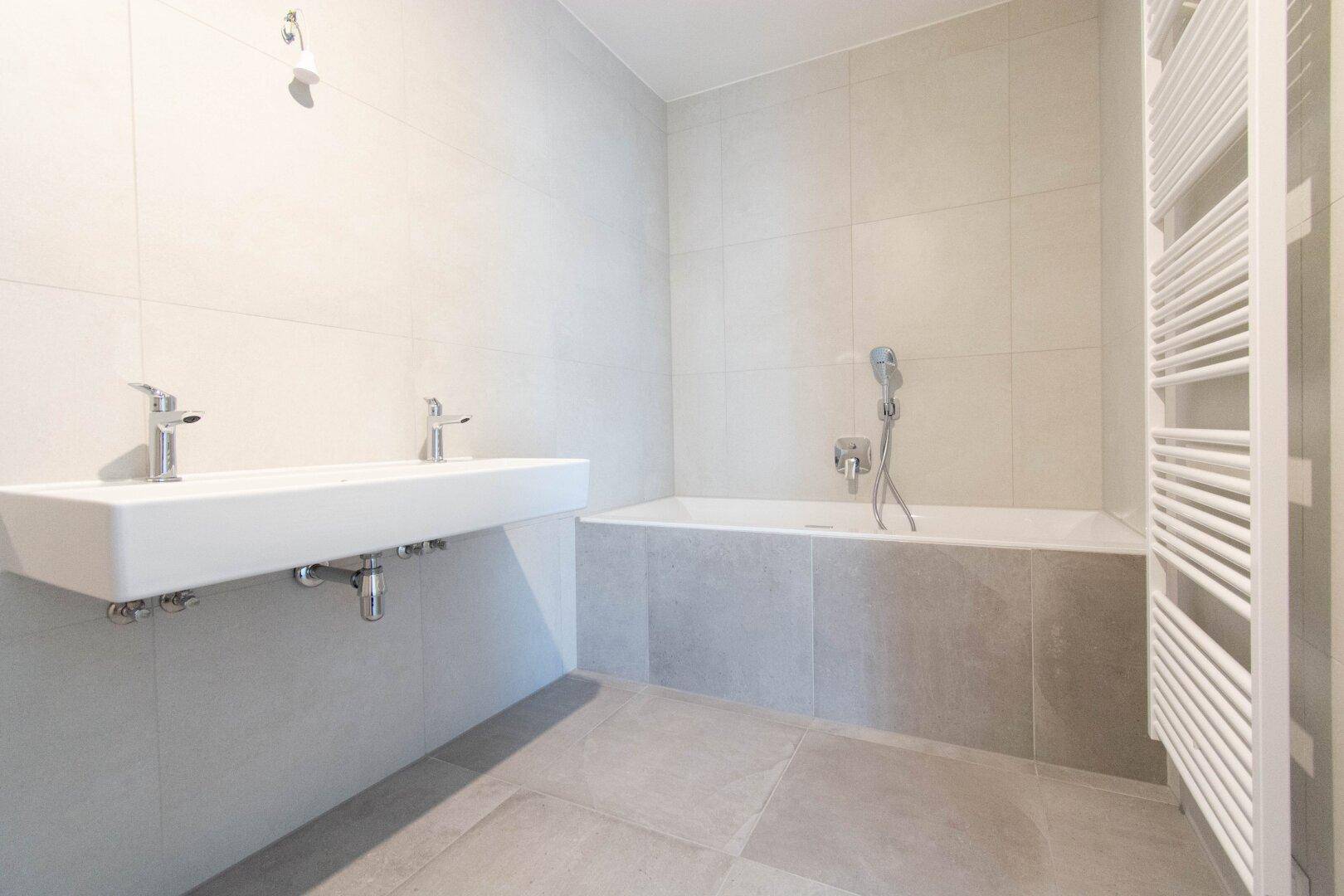 Modernes Badezimmer mit Doppelwaschbecken, Badewanne und hellen Fliesen.