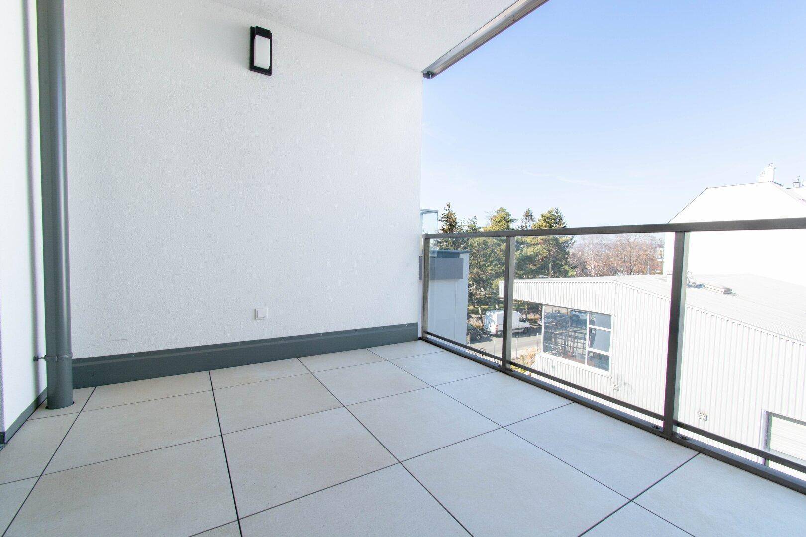 Geräumiger Balkon mit Fliesenboden und Glasgeländer, bietet einen Blick auf die Umgebung.