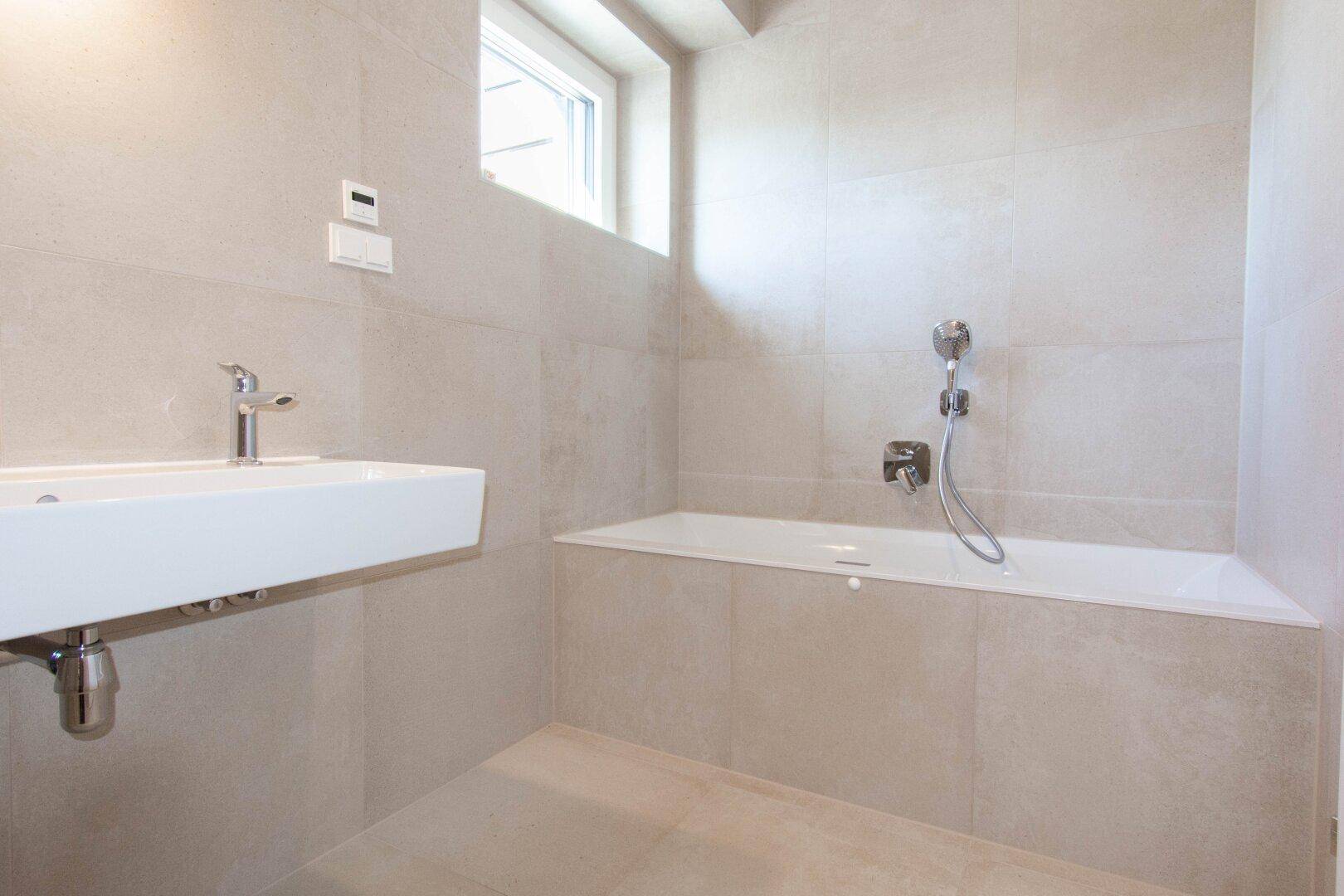 Helles Badezimmer mit Badewanne, modernem Waschbecken und kleinem Fenster für Tageslicht.