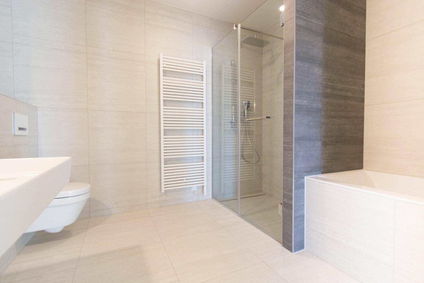 Modernes Badezimmer mit großformatigen Fliesen, begehbarer Dusche und beheiztem Handtuchhalter.