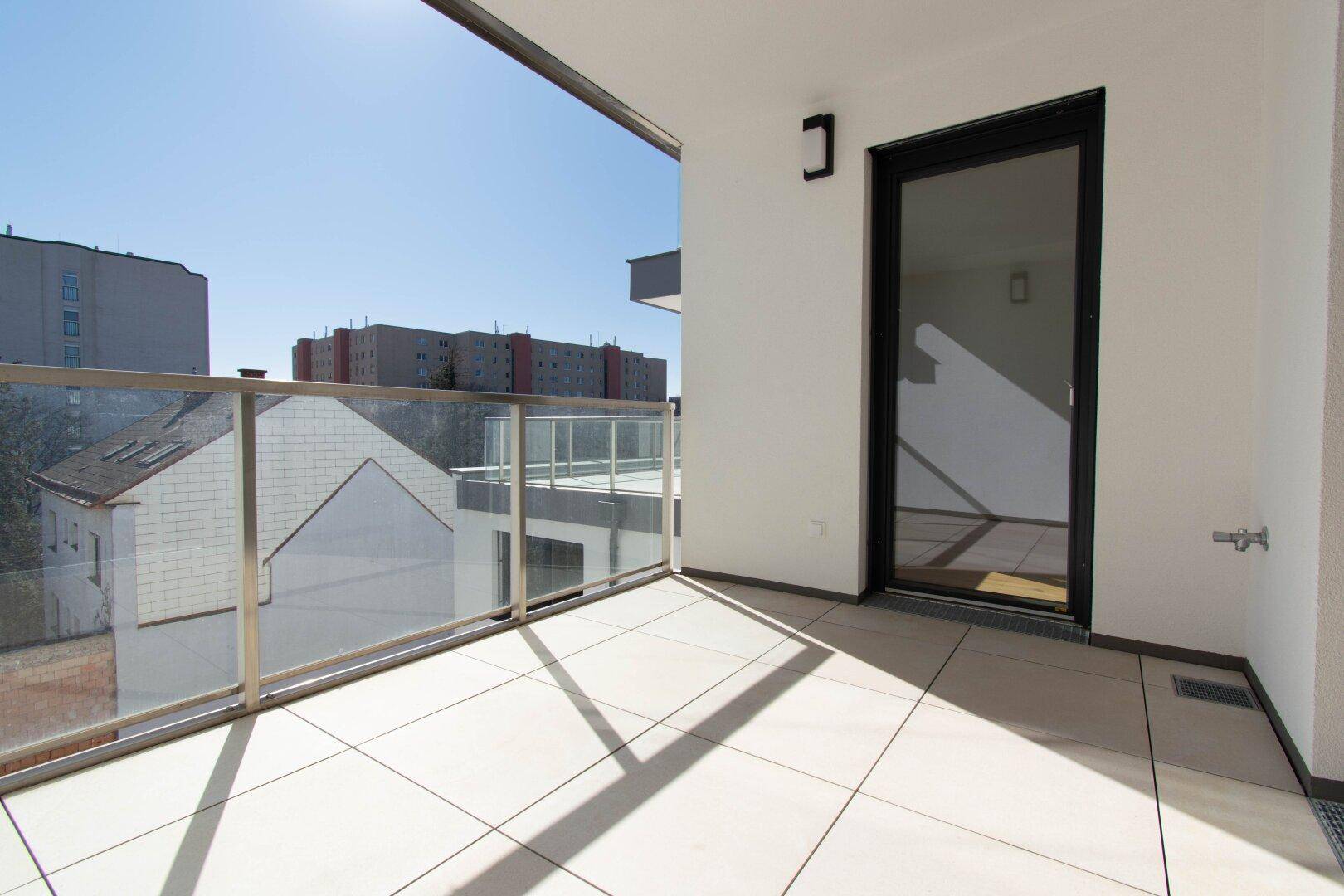 Sonniger Balkon mit Glasgeländer und Blick auf die umliegenden Gebäude, ideal für Morgenkaffee.