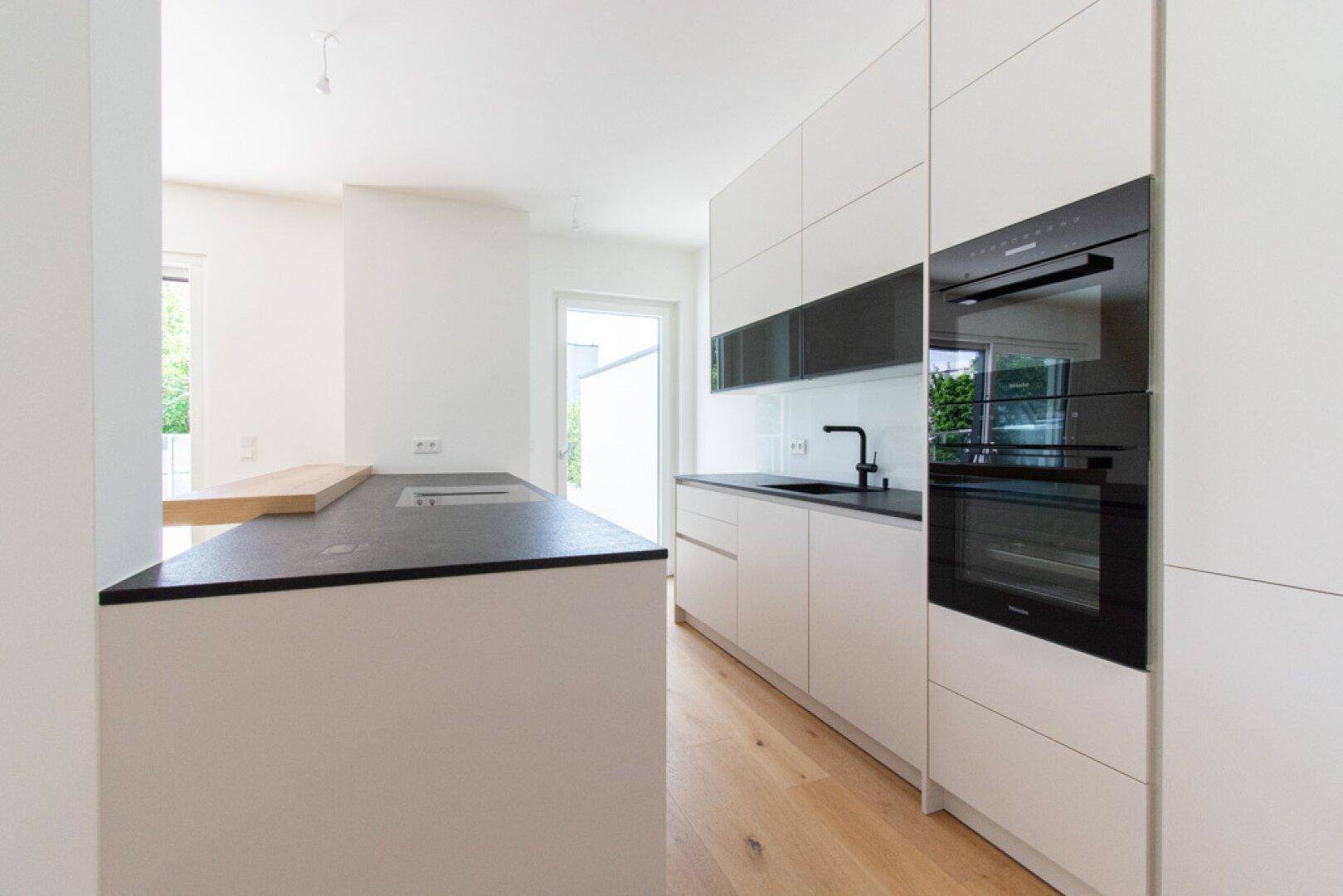 Moderne Einbauküche mit Kücheninsel, schwarzen Arbeitsplatten und integrierten Geräten.