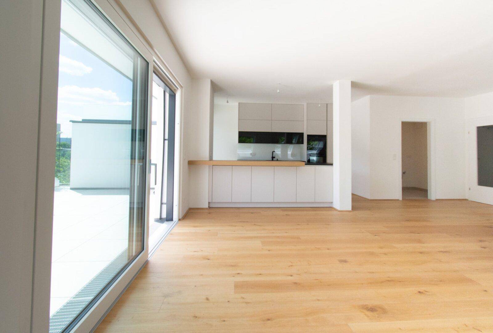 Heller offener Wohnbereich mit Holzboden und integrierter moderner Küche, Zugang zur Terrasse.