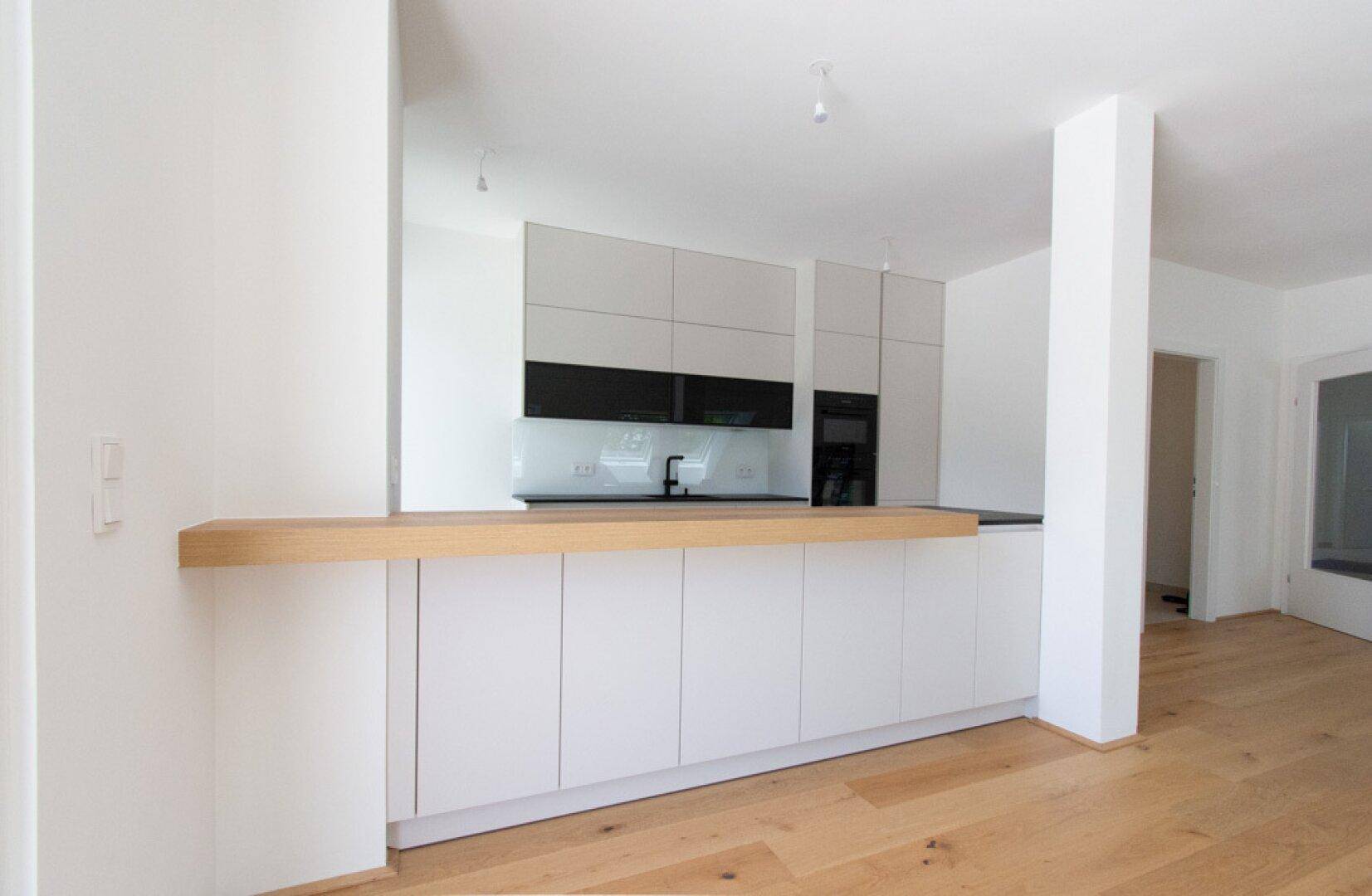 Moderne Einbauküche mit weißen Fronten, Holzarbeitsplatte und integrierter Frühstücksbar.