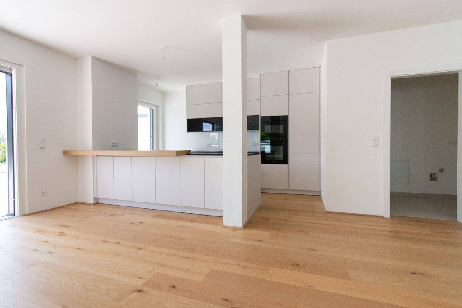 Heller offener Wohnbereich mit Holzboden und integrierter moderner Küche, Zugang zur Terrasse.