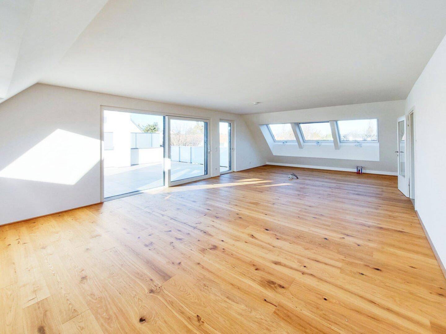 Heller, leerer Raum mit Holzboden, großen Schiebetüren zur Terrasse und Dachfenstern.