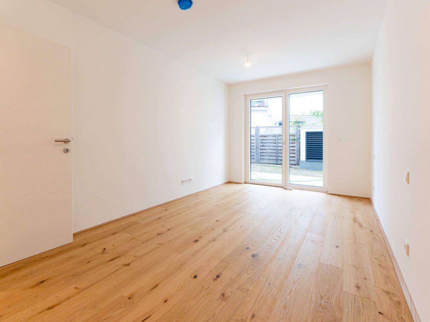 Leeres Zimmer mit Holzboden und Zugang zu einem kleinen Außenbereich, ideal als Schlafzimmer.