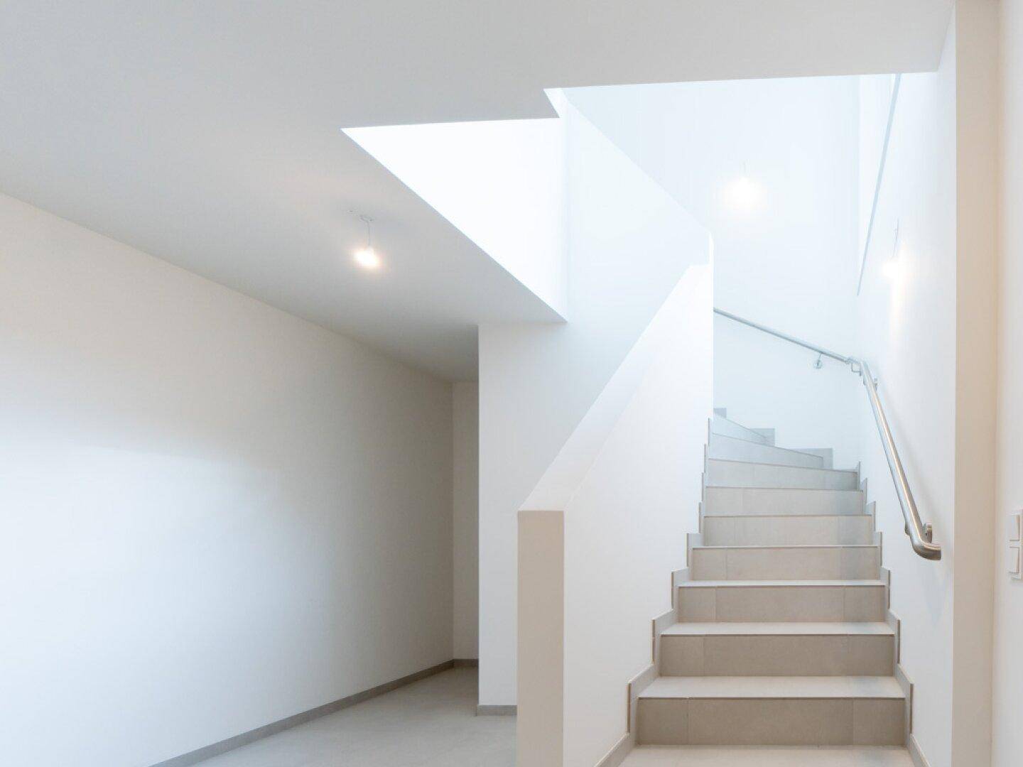 Moderne Treppe mit Fliesenstufen und schlichtem Geländer, die die Etagen verbindet.