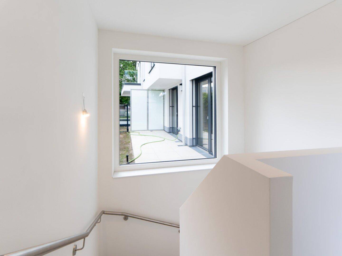 Treppenabsatz mit Fenster, das einen Blick auf die Außenterrasse und den Gartenbereich bietet.
