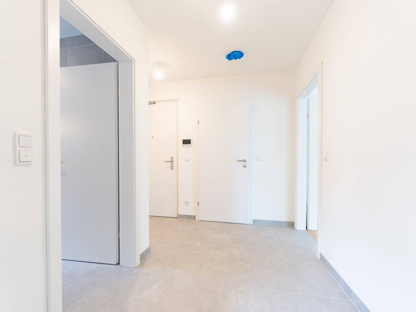 Heller Flur mit modernen grauen Fliesen und mehreren weißen Türen zu den angrenzenden Zimmern.