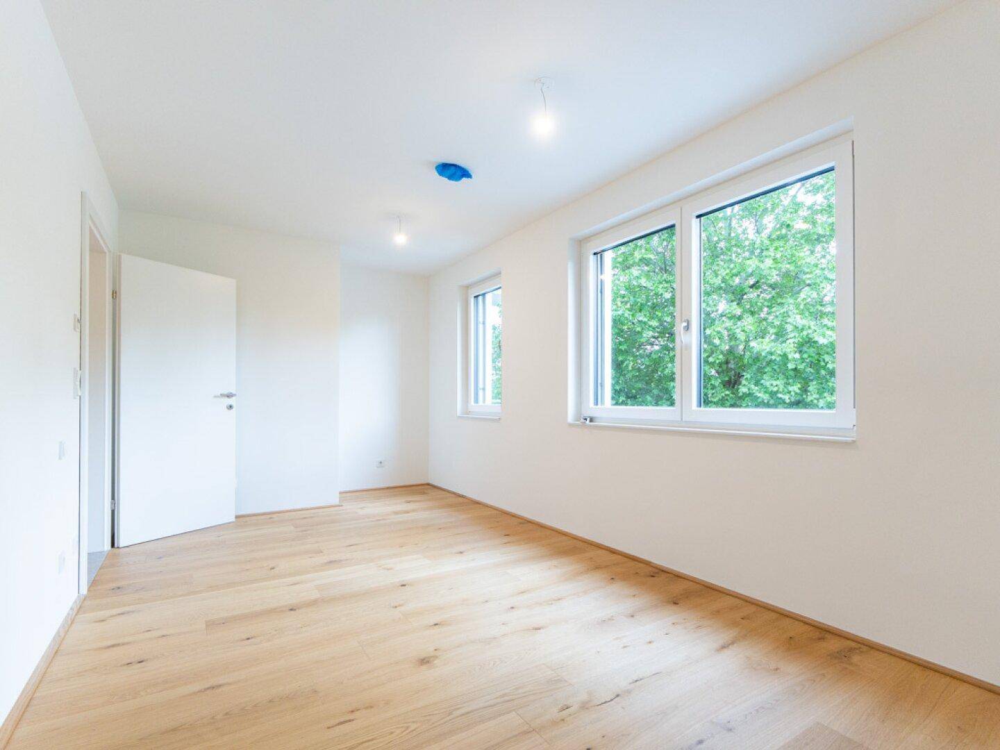 Helles Zimmer mit neuem Holzparkettboden und Blick ins Grüne durch große Fenster.