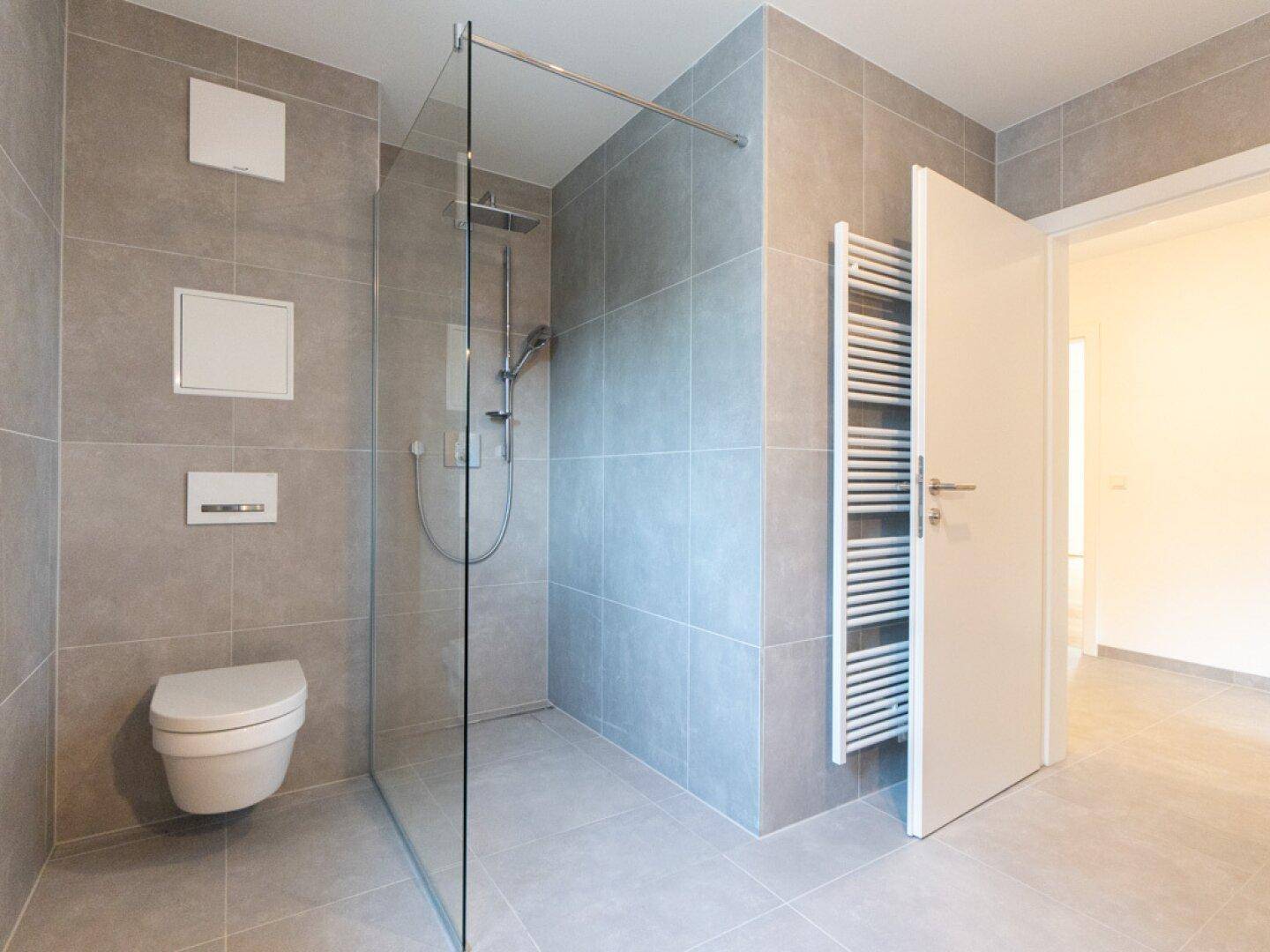Modernes Badezimmer mit grauen Fliesen, ebenerdiger Dusche und wandhängendem WC.