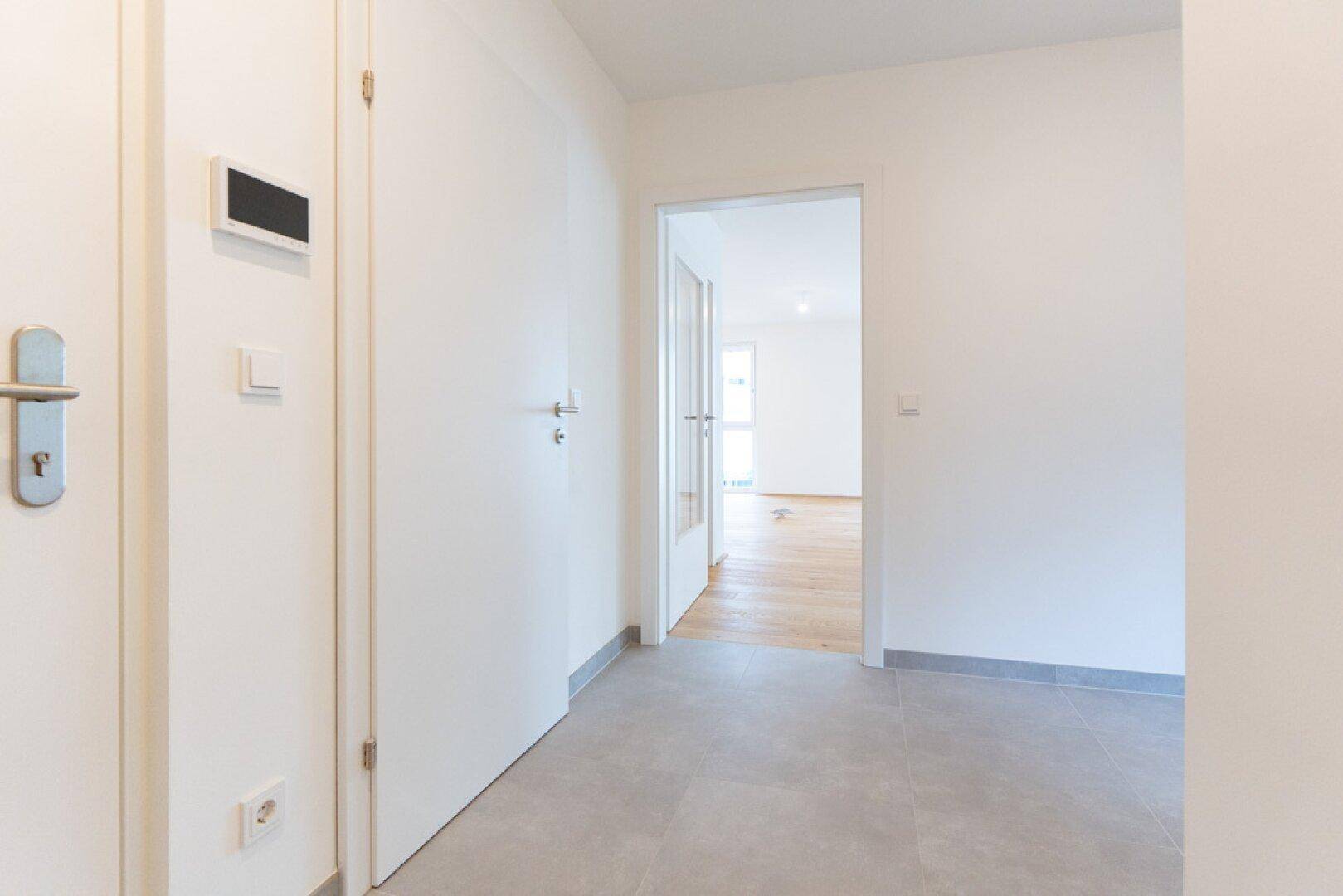 Heller Flur mit modernen grauen Fliesen und mehreren weißen Türen zu den angrenzenden Zimmern.