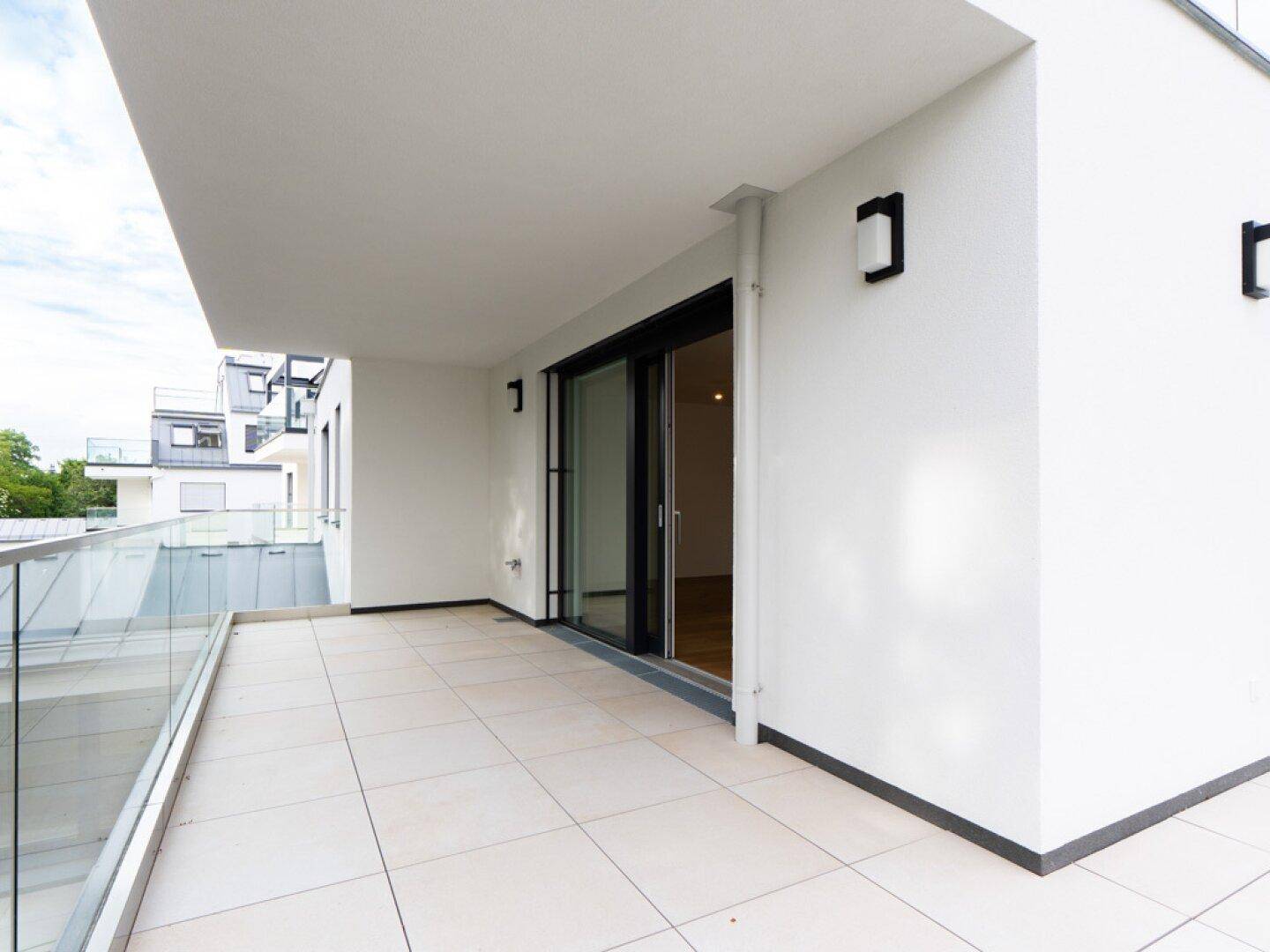 Geräumige Terrasse mit modernen Fliesen und Glasgeländer, ideal für entspannte Stunden im Freien.