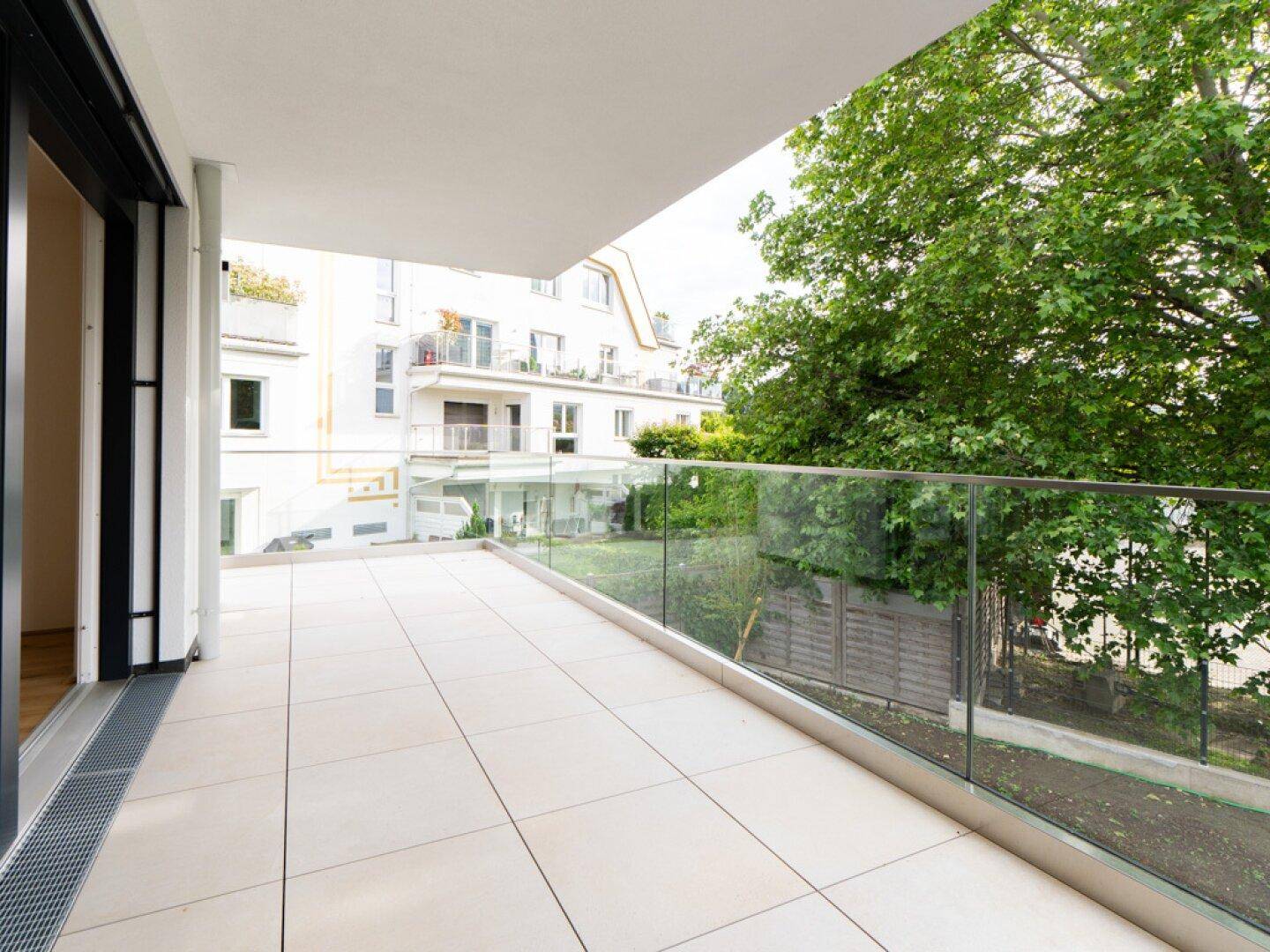 Moderne Terrasse mit Glasgeländer und Blick auf den Garten sowie umliegende Gebäude.