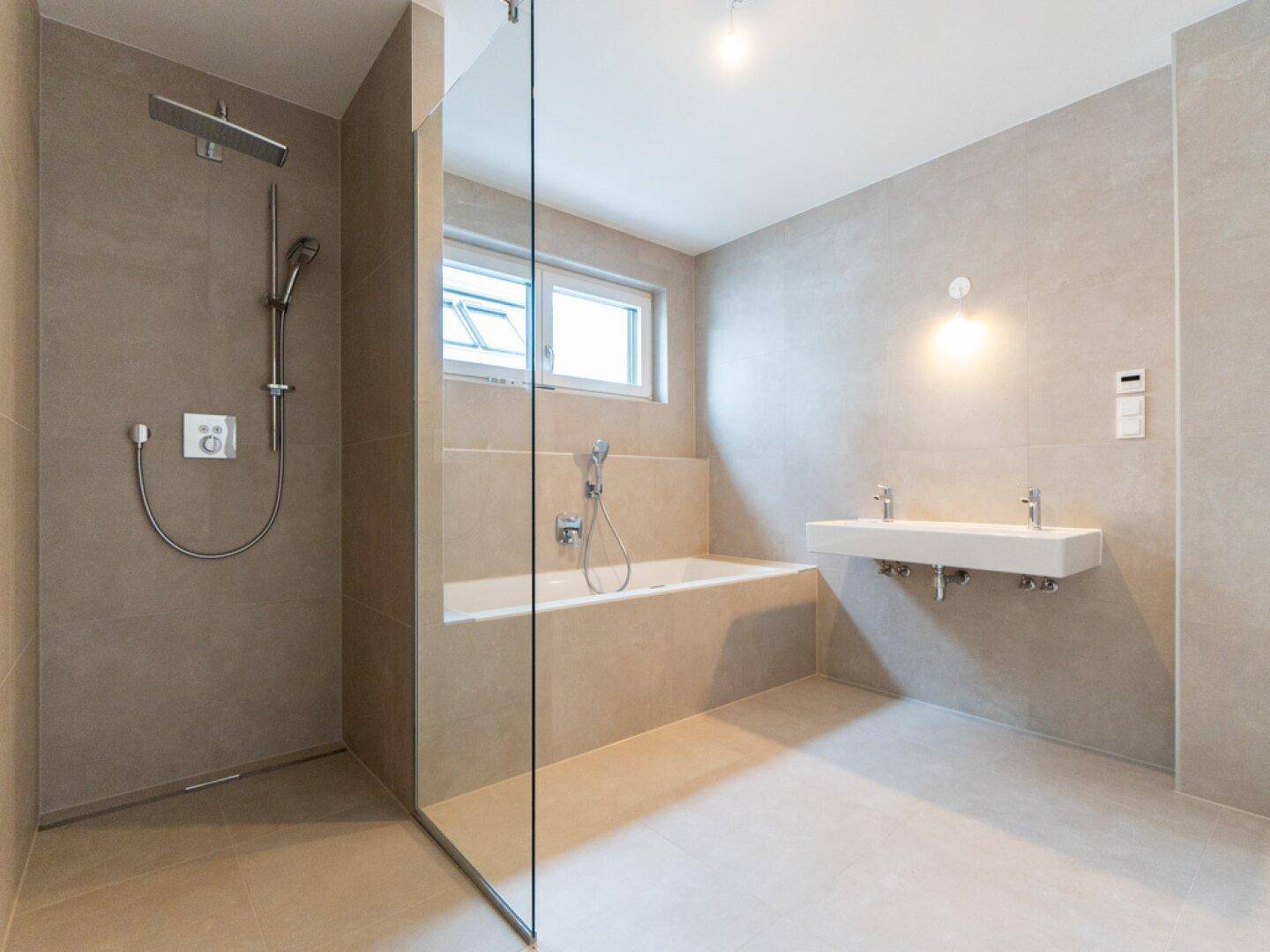 Modernes Badezimmer mit hellgrauen Fliesen, begehbarer Dusche, Badewanne und Doppelwaschbecken.