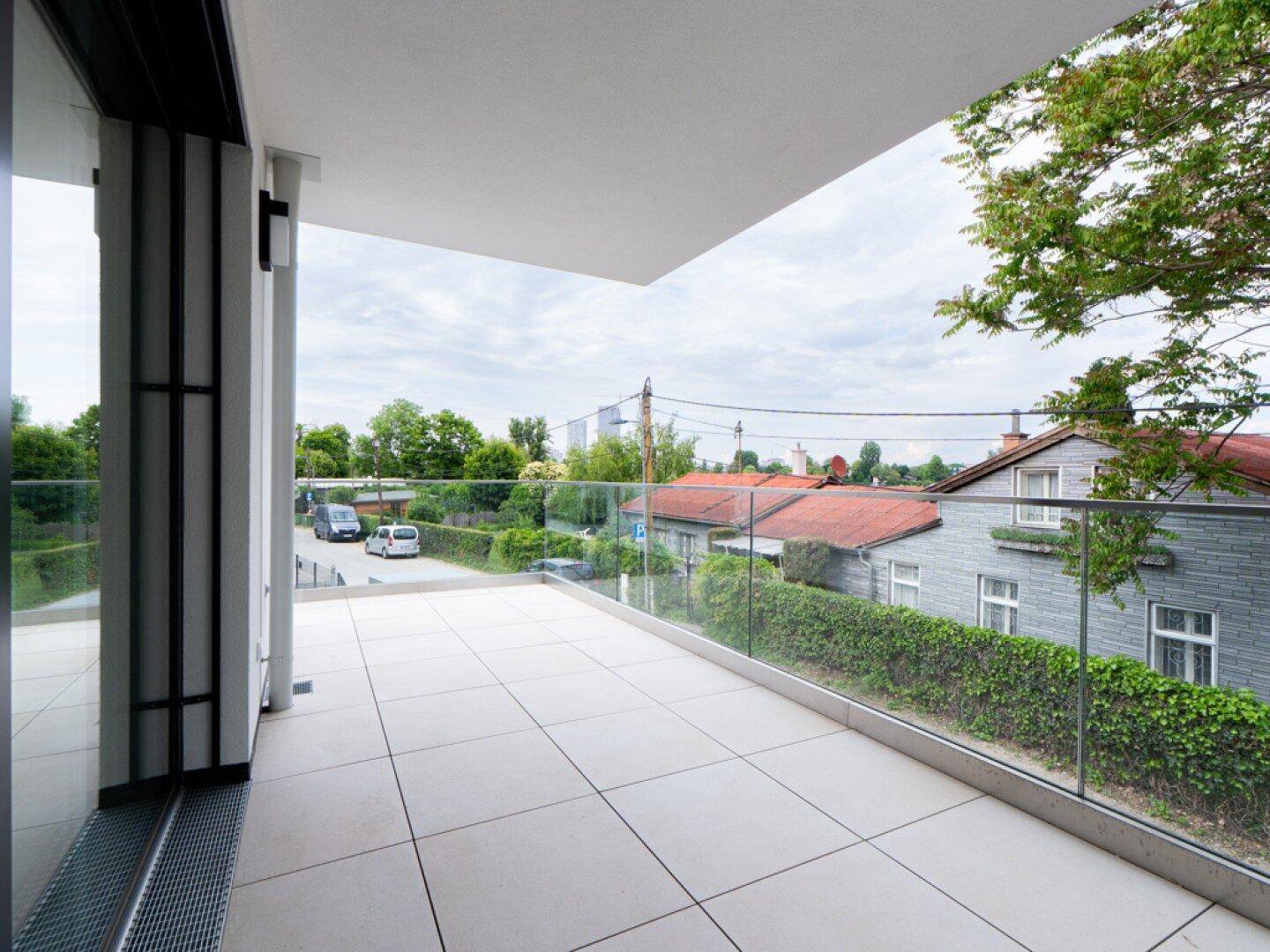 Geräumiger Balkon mit Fliesenboden, Glasgeländer und Blick auf die Nachbarschaft.