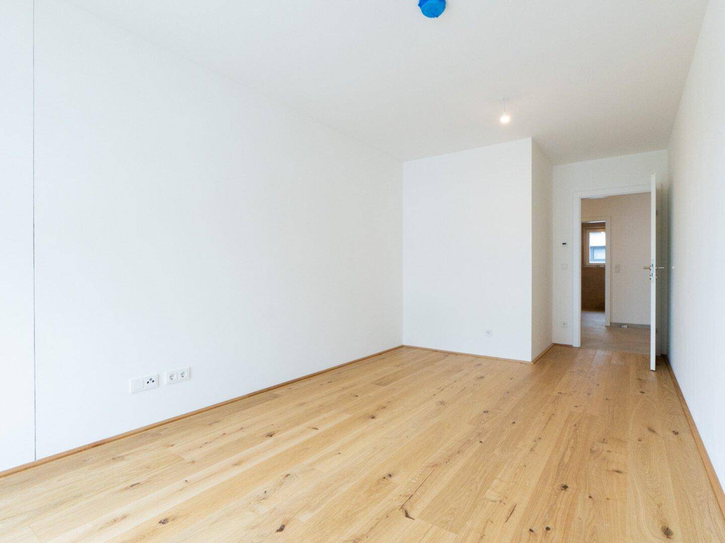 Leeres Zimmer mit hellem Eichenparkett und weißen Wänden, ideal als Schlaf- oder Arbeitszimmer.