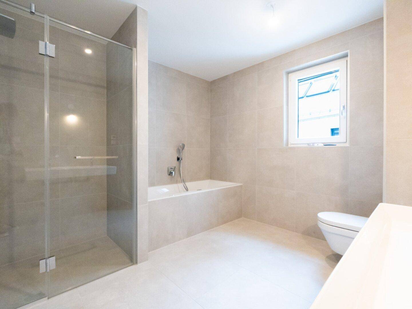 Modernes Badezimmer mit beigen Fliesen, Badewanne, ebenerdiger Dusche und Fenster.