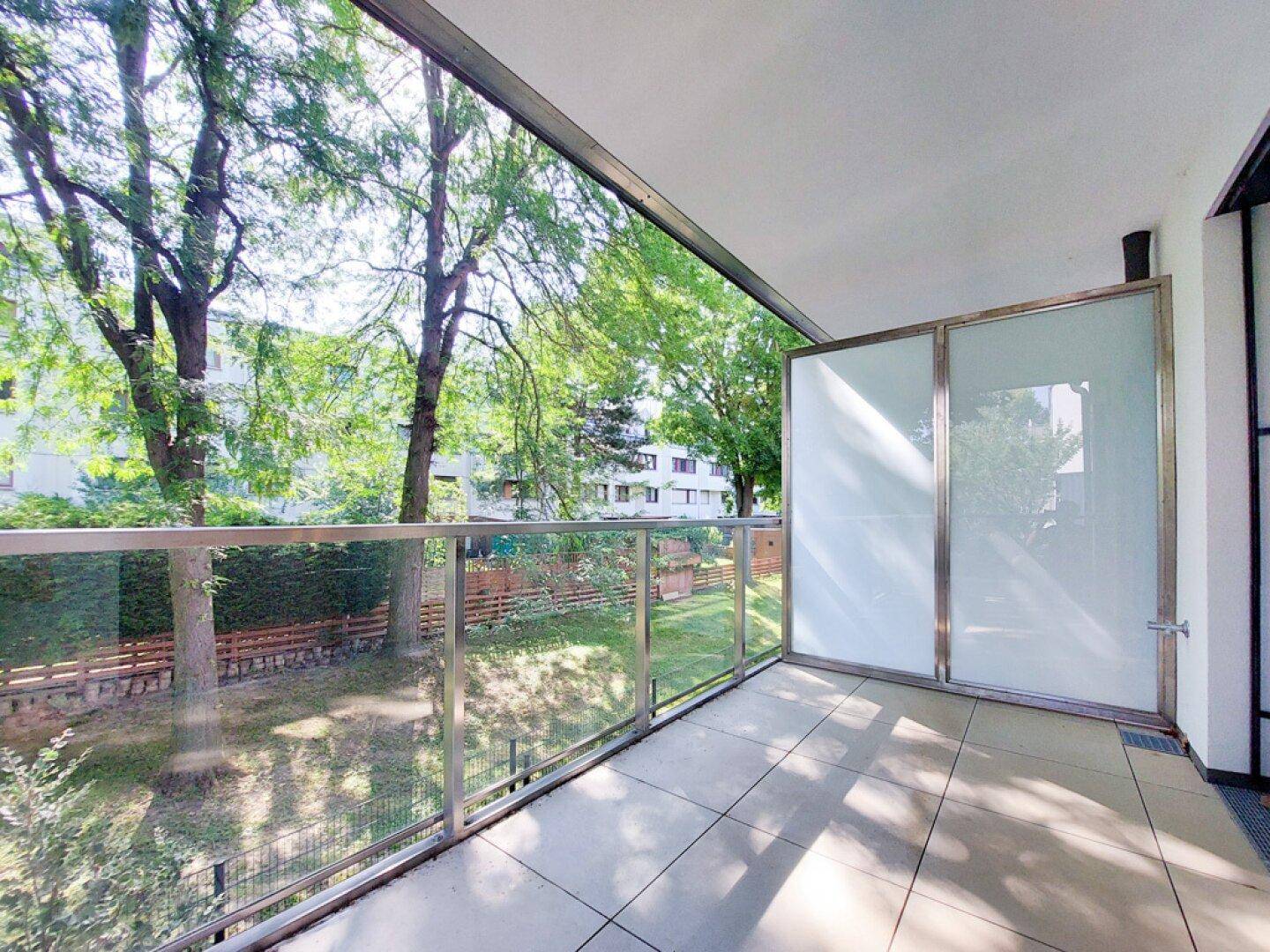 Moderner Balkon mit Glasgeländer und Blick ins Grüne, perfekt zum Entspannen.